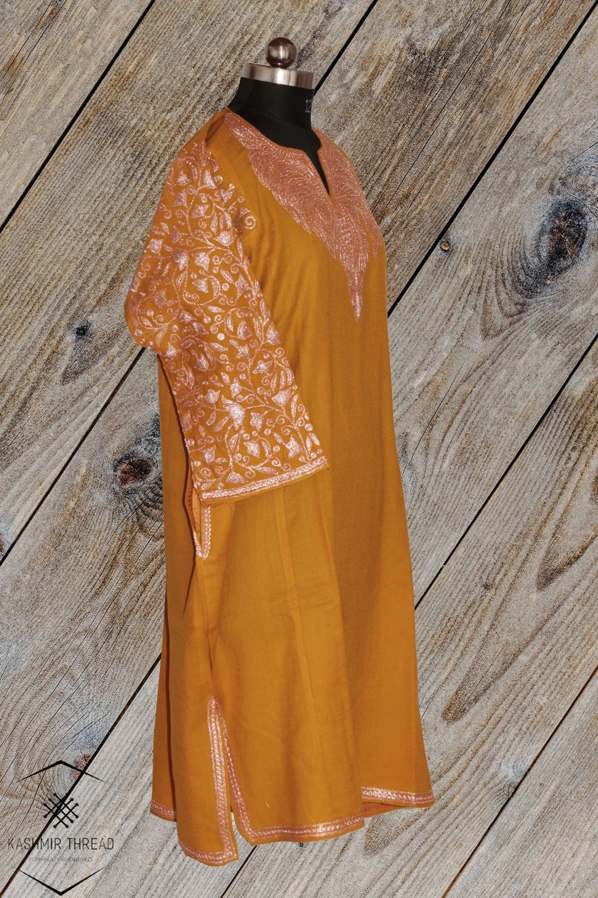 Three-quarter view of mustard pheran with pale pink Tilla embroidered neckline and sleeves, side slit and narrow hem trim