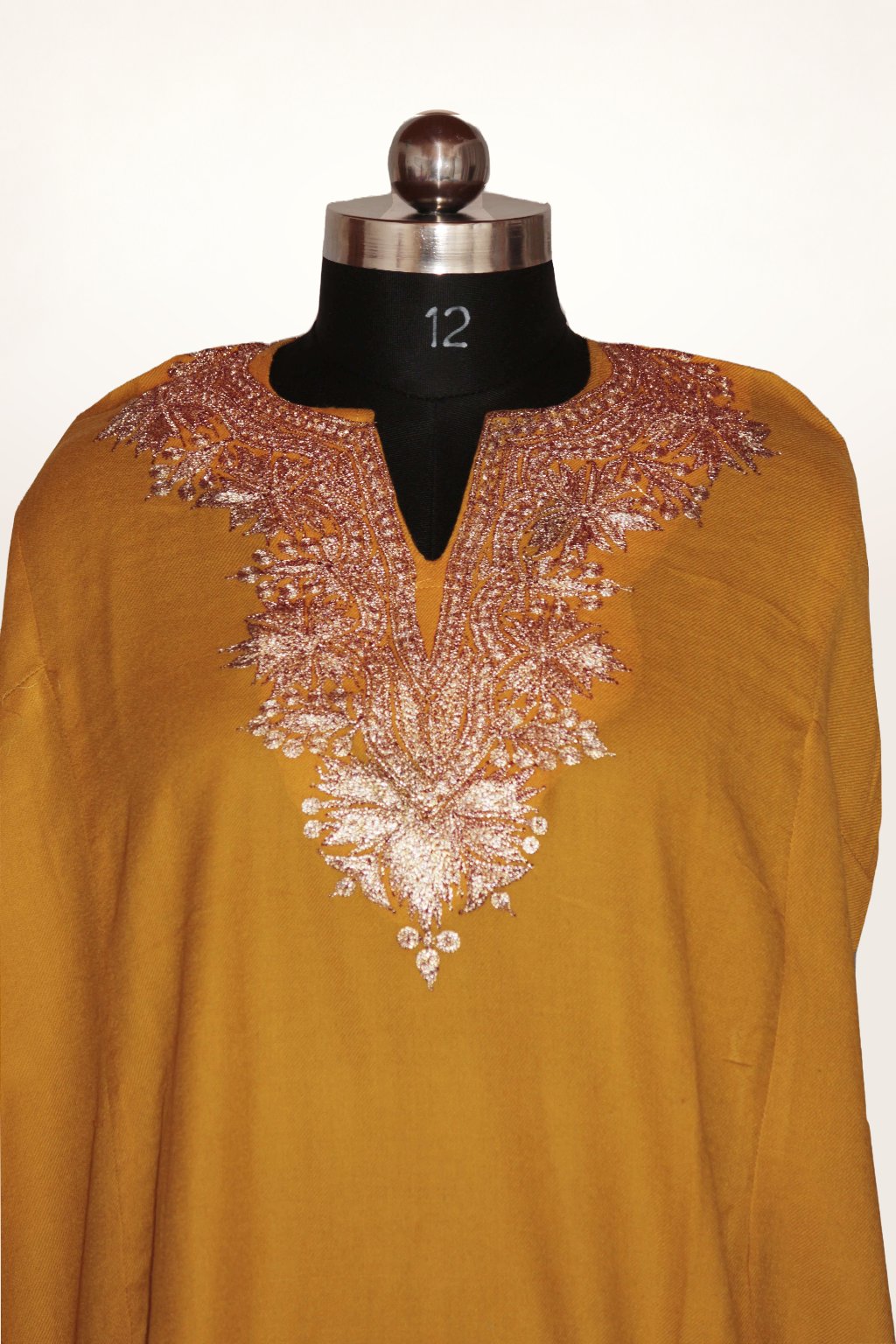 Front close-up of a mustard pheran on a mannequin, with pale metallic Tilla floral embroidery framing the split neckline.