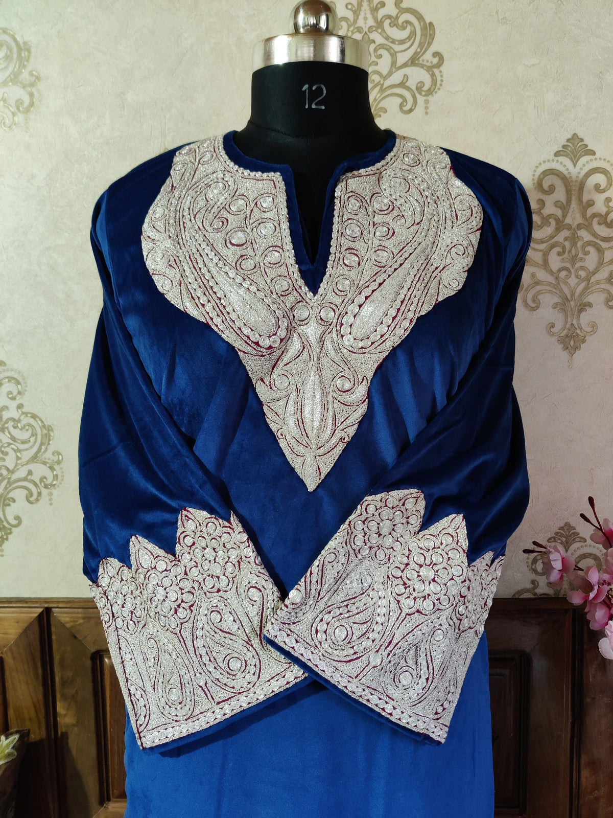 Front detail of a blue velvet pheran, with dense silver-toned Tilla paisley embroidery around the neckline and on crossed cuffs.