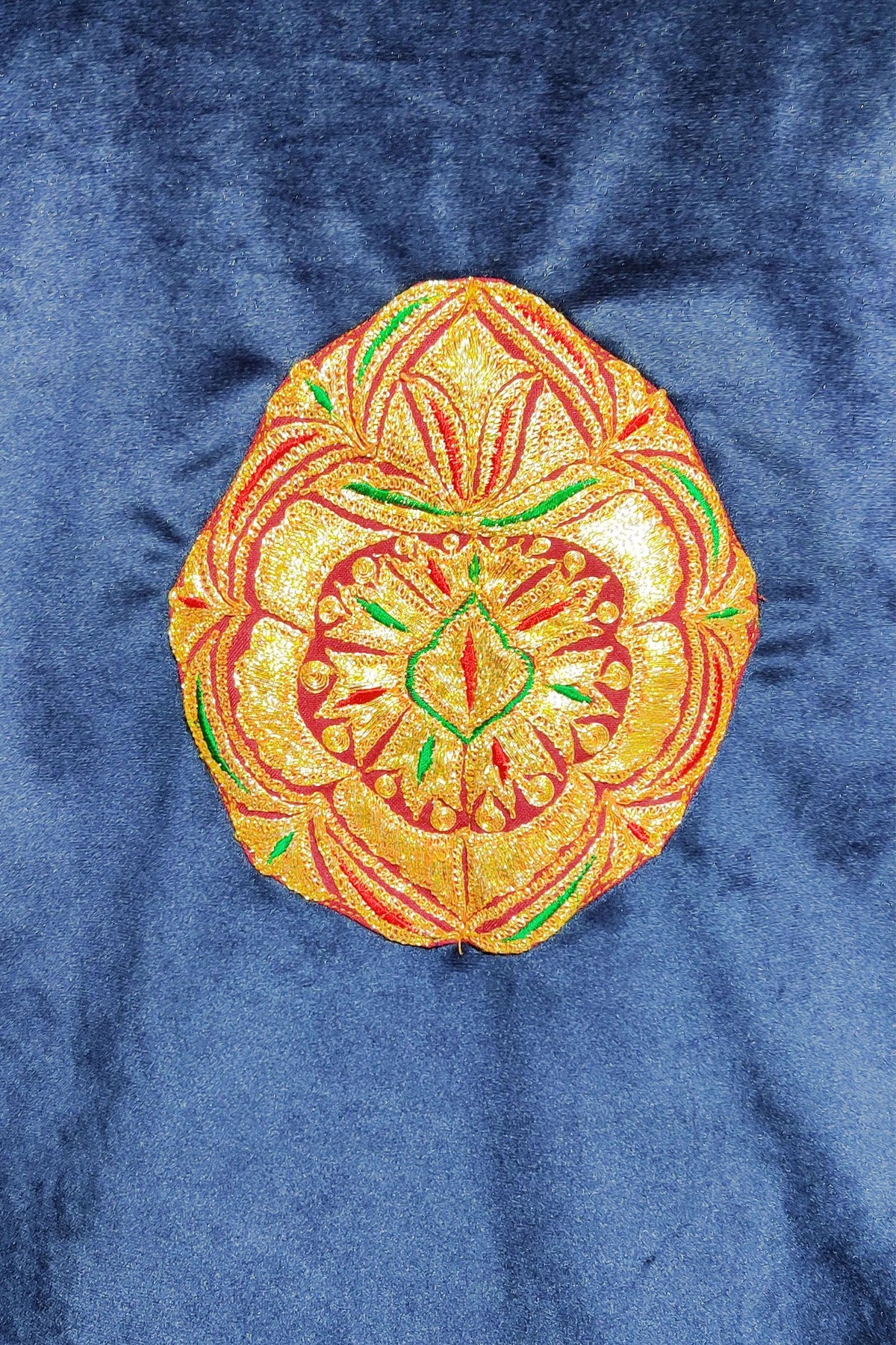 Round gold-toned floral motif with red and green details embroidered on blue velvet.