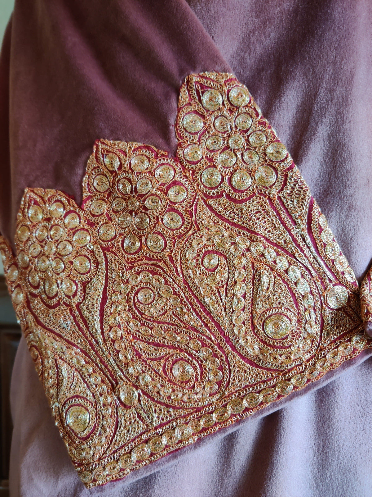 Detailed view of a dusty pink velvet cuff with gold-toned Tilla paisleys, round rosettes and fine scrolling stitches