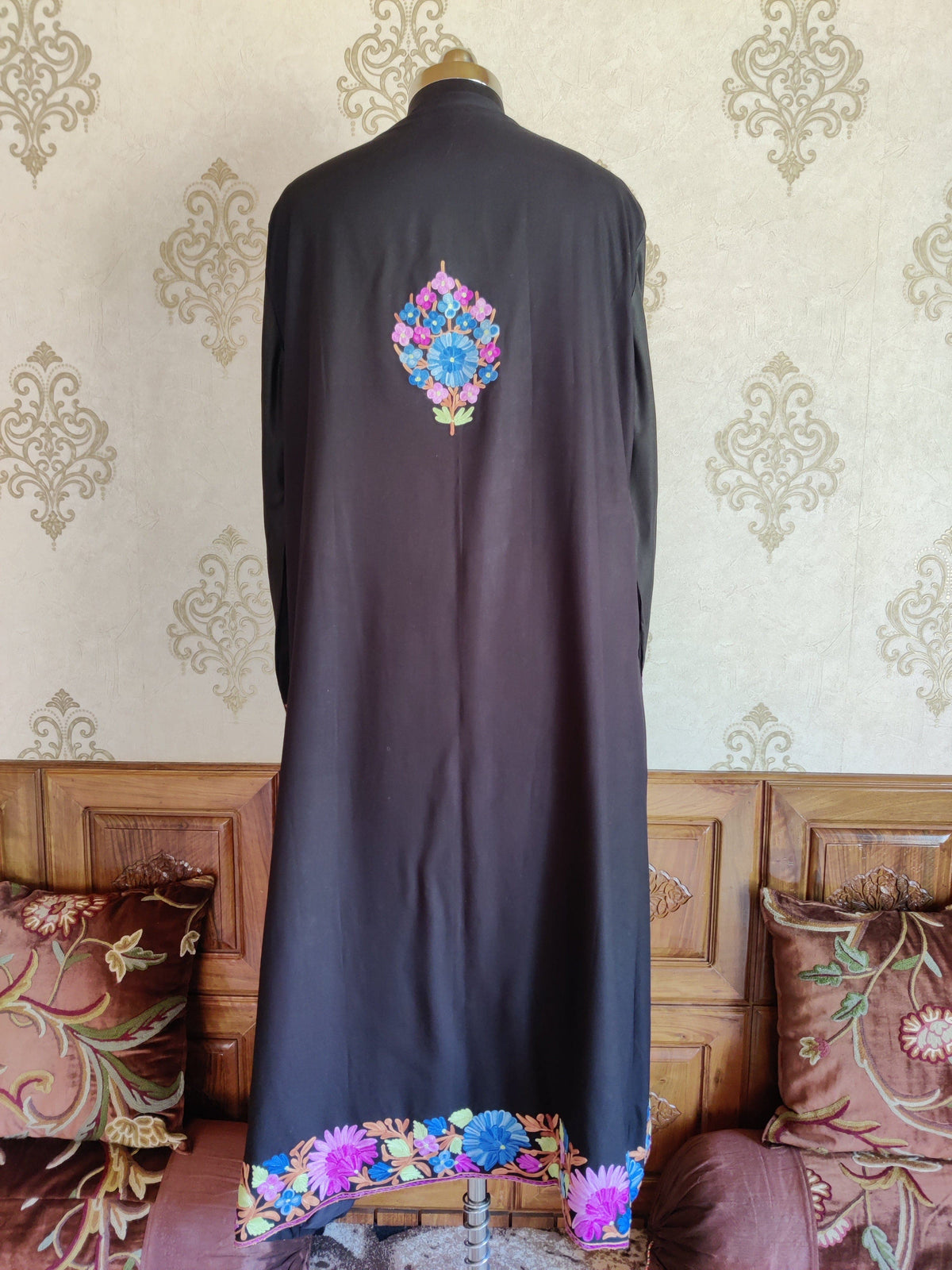 Back of a black robe with a small blue and purple floral bouquet high on the back and a colourful floral hem border.