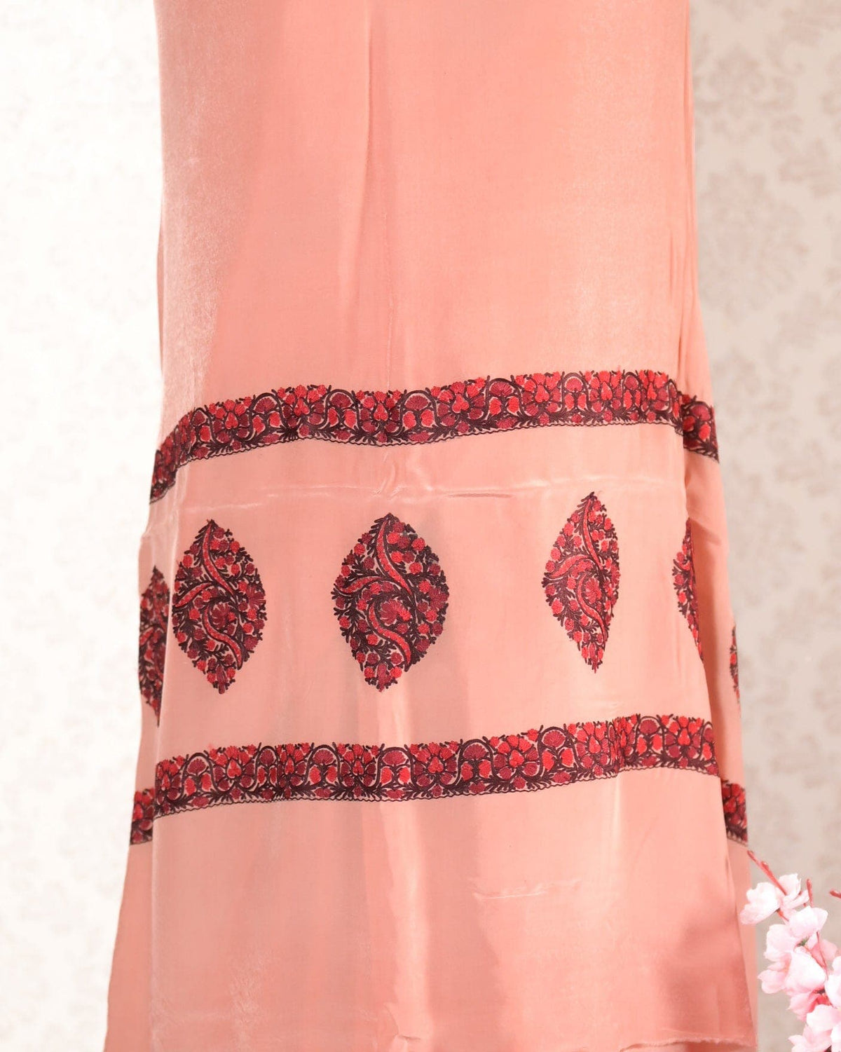 Close-up of the peach crepe saree end, with red and black leaf-shaped Aari motifs between two floral embroidered bands