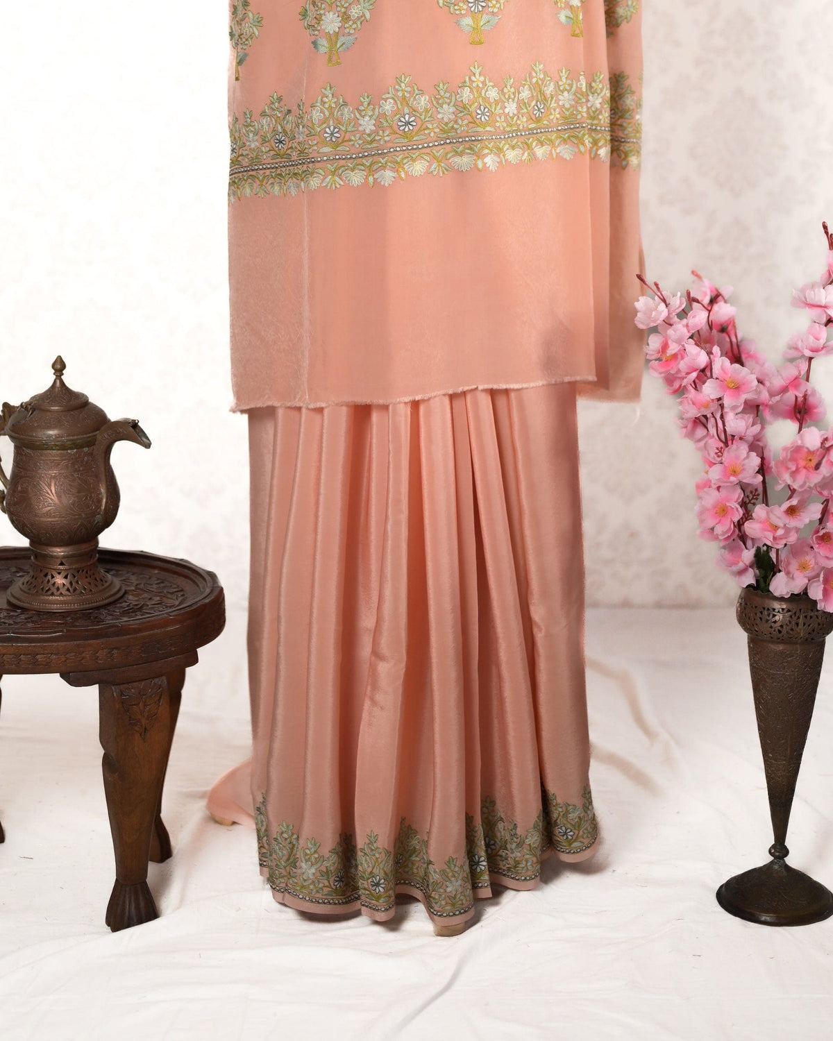 Lower pleated drape of a peach crepe saree with pale green Aari floral edging, beneath the embroidered pallu end