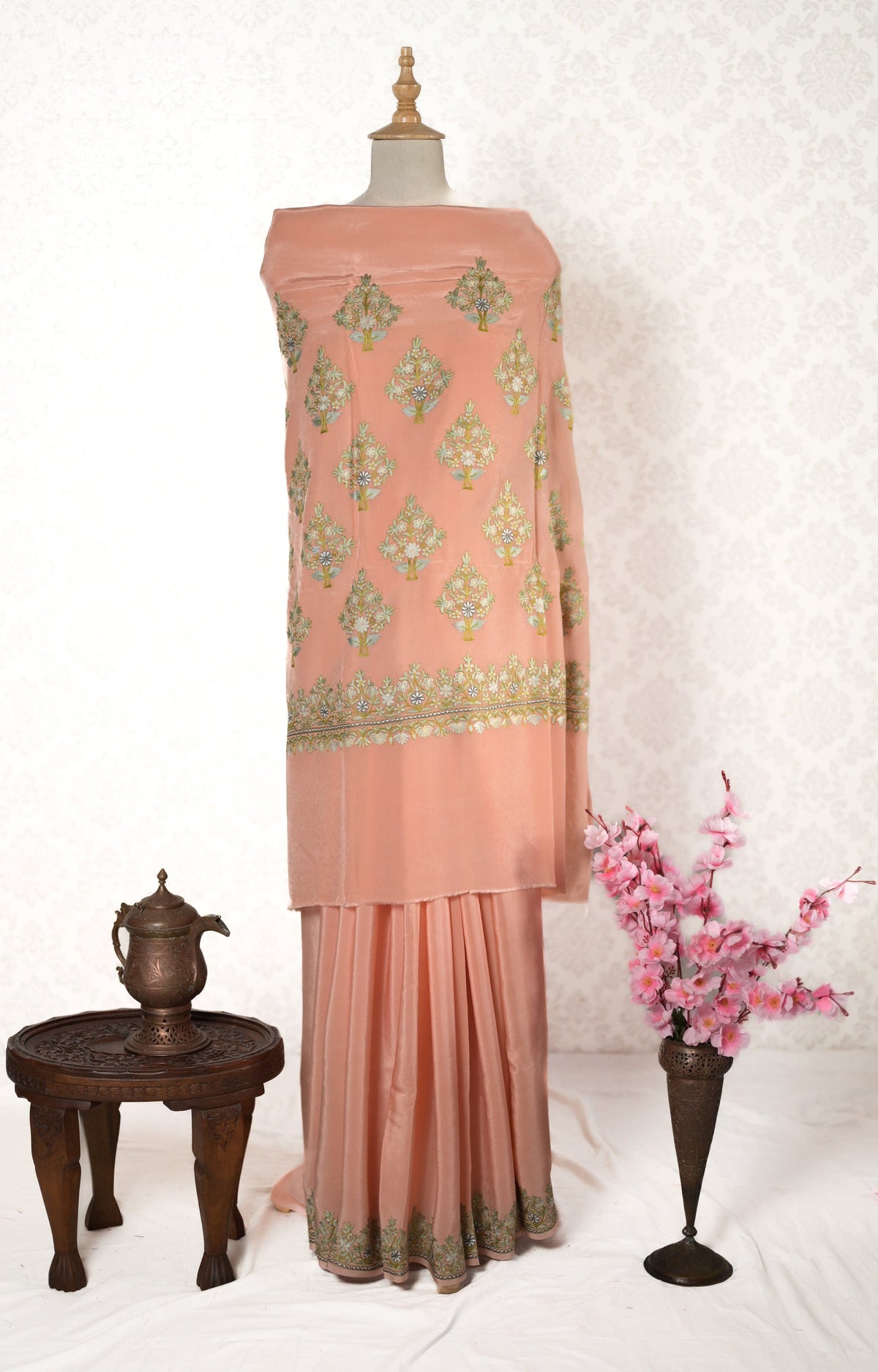 Full view of a peach crepe saree on a mannequin, with floral-embroidered pallu above plain pleats and a decorated hem