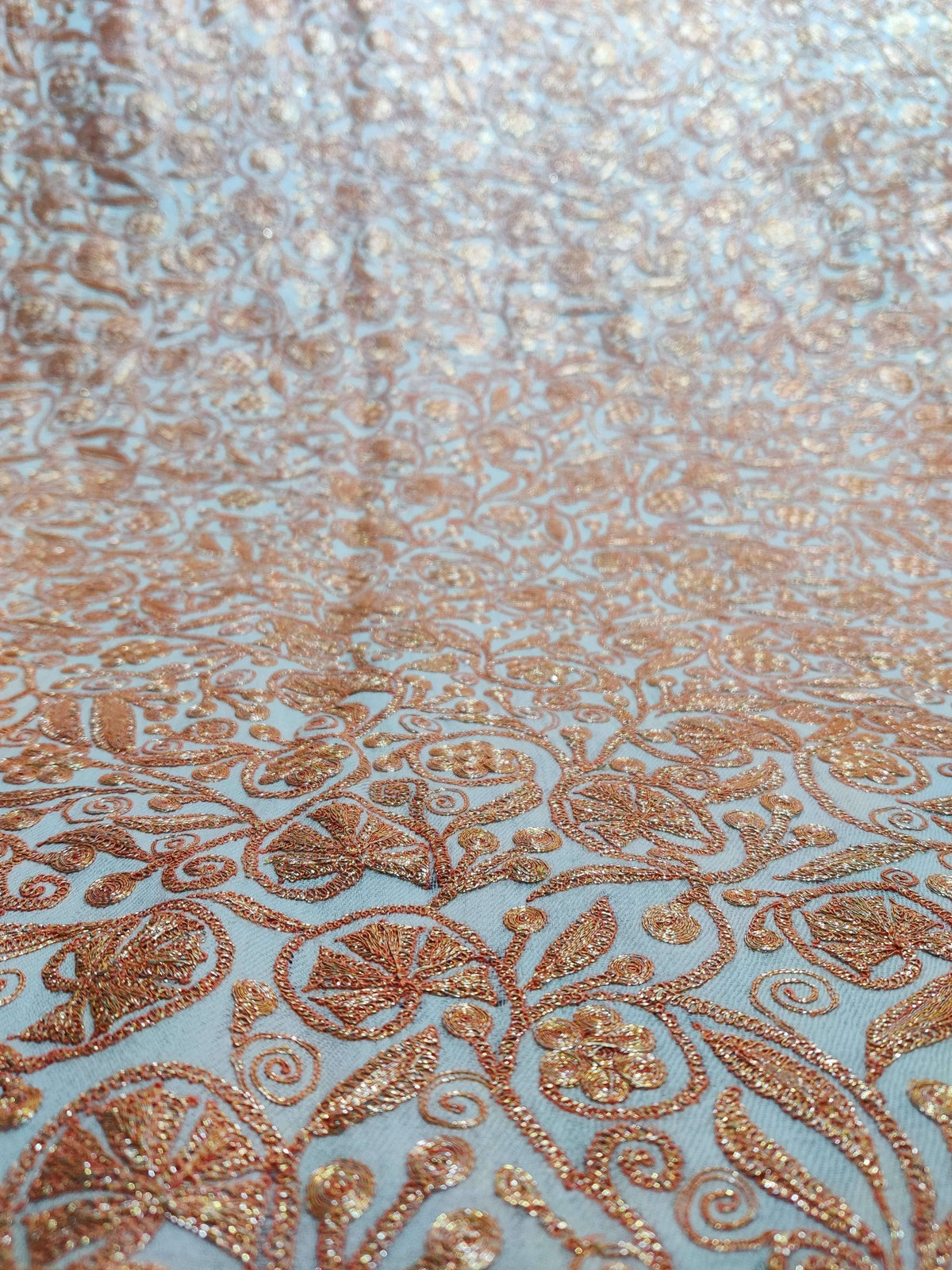 Macro view of golden-peach Tilla flowers and curled leafy stems across white Merino wool fabric