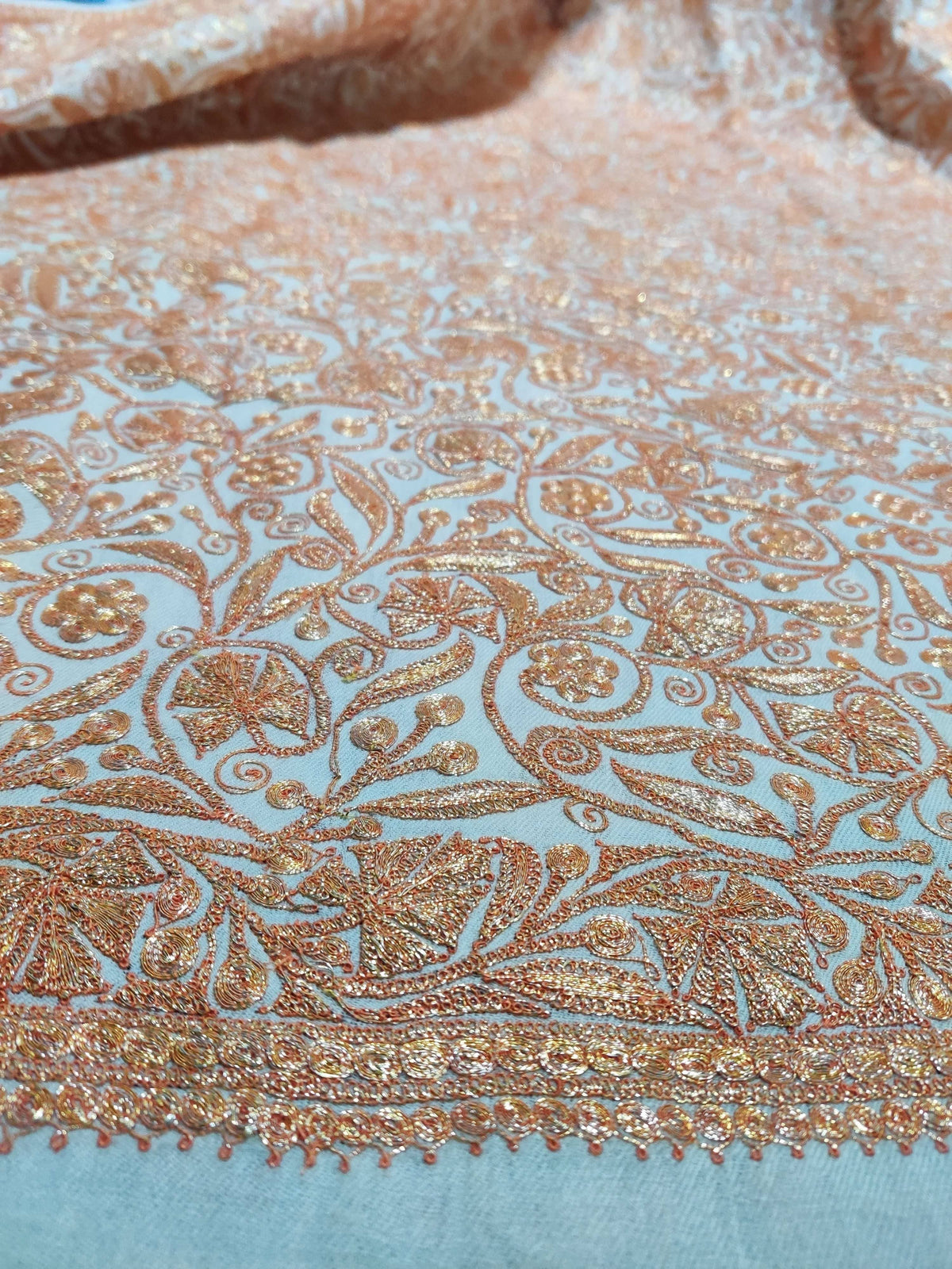 Angled close-up of golden-peach Tilla flowers and curling stems meeting the embroidered edge of a white Merino wool shawl