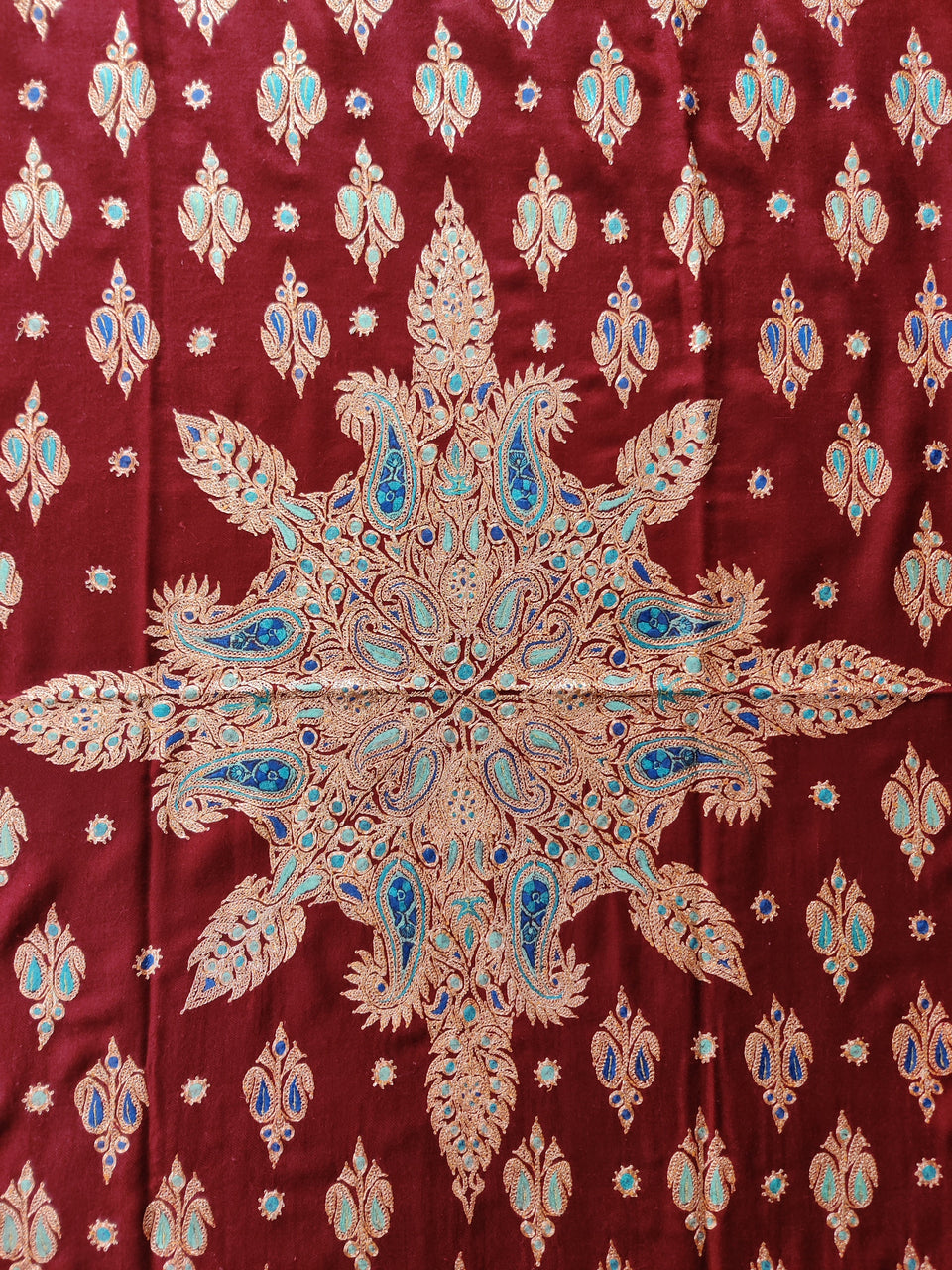 Red fabric with an ornate gold-coloured and blue central medallion surrounded by small floral motifs