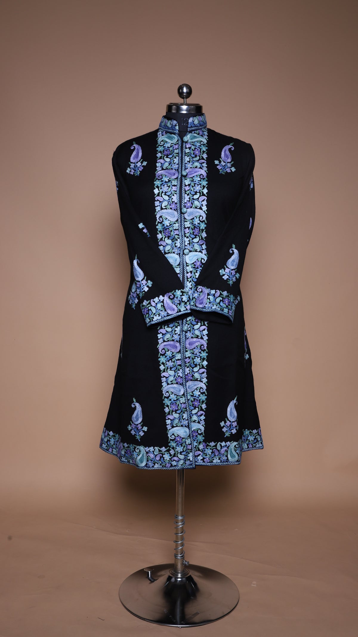 Full-length studio view of the black Paisley Elegance jacket on a mannequin, with blue-purple borders and crossed sleeves.