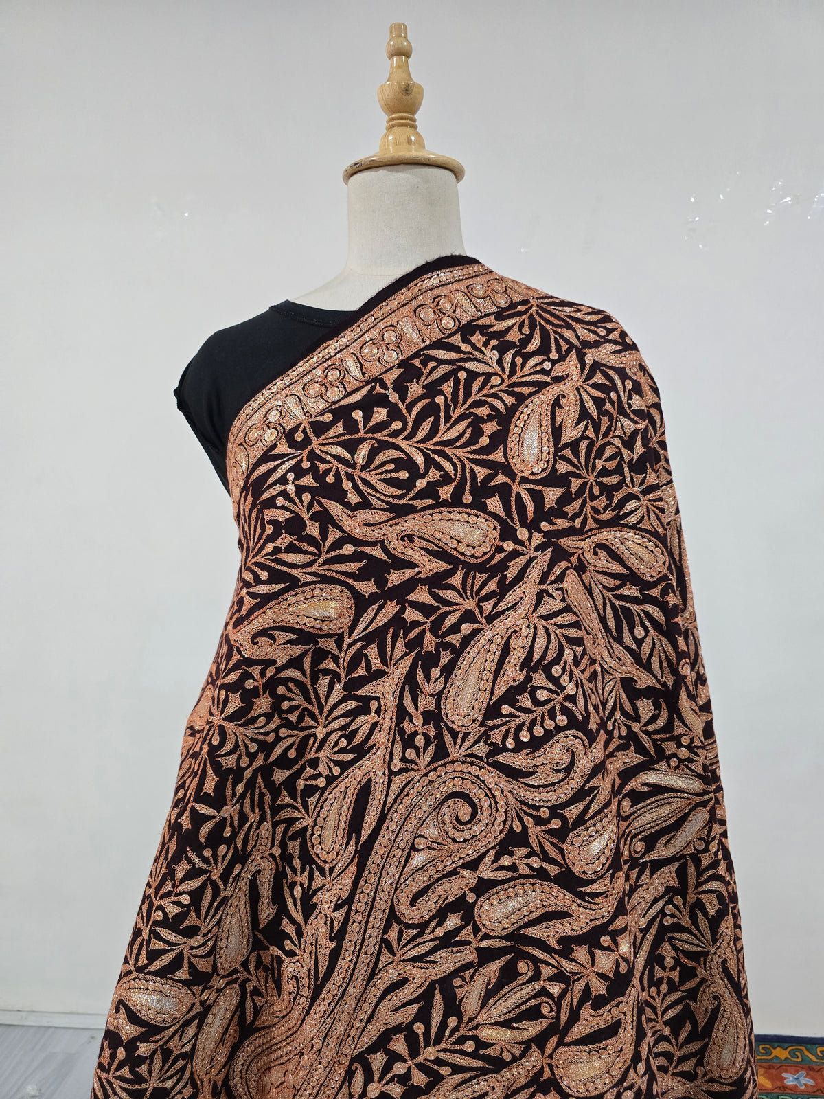 Mid-length draped view of the brown shawl with a large sweeping paisley among smaller copper-gold motifs and leafy vines.