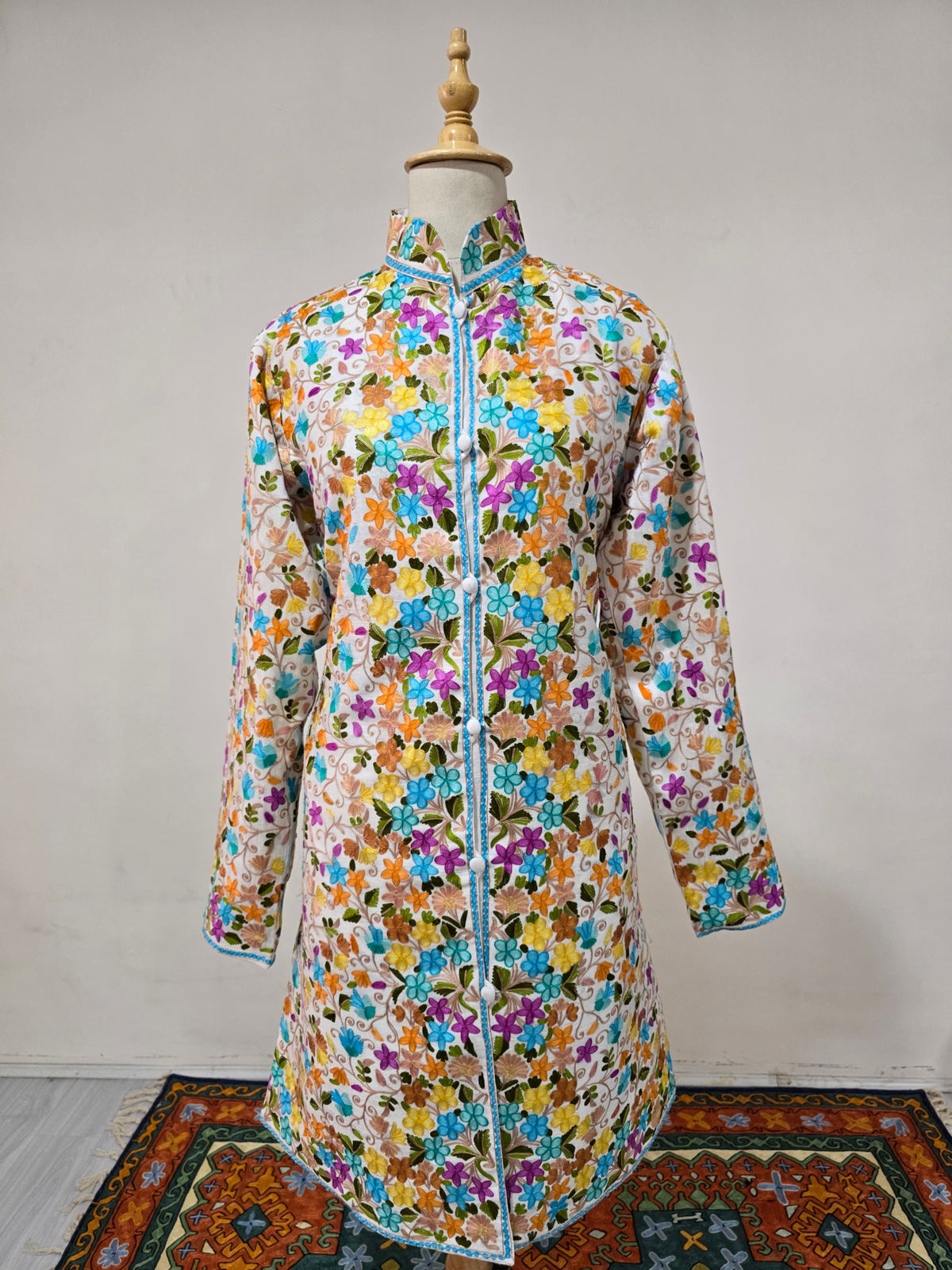 Full front view of the white long jacket with long sleeves, a fitted waist and all-over colourful Aari floral embroidery.