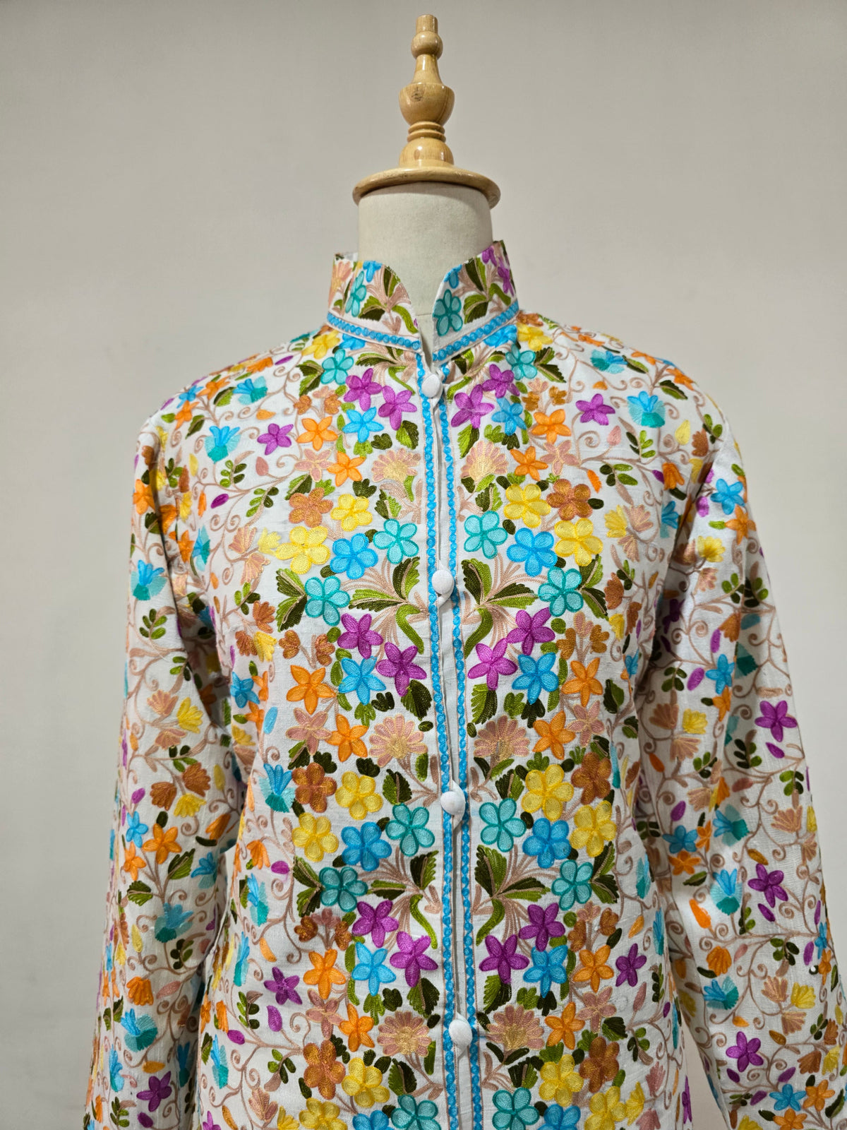 Front view of the jacket upper body, showing bright embroidered flowers, green leaves and a blue-edged stand collar.