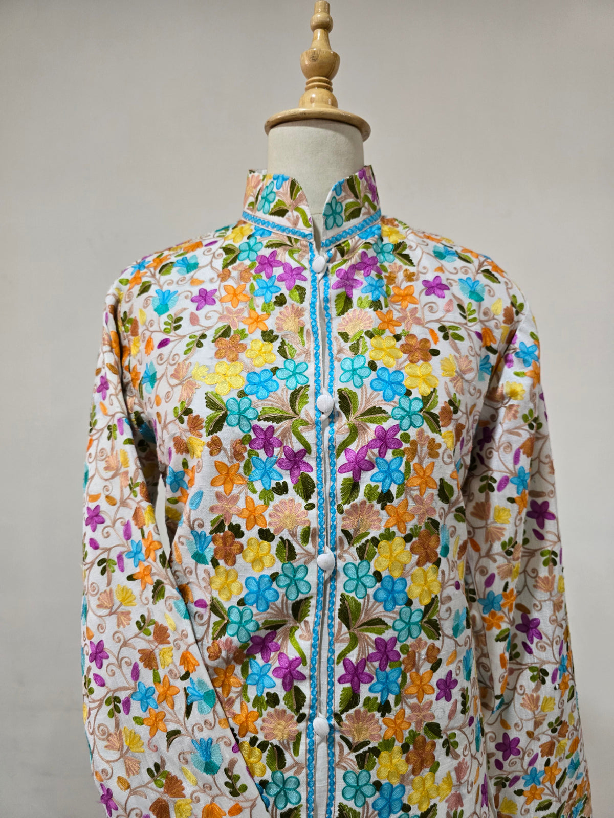 Upper front of the white jacket with a stand collar, white covered buttons and dense multicoloured floral embroidery.