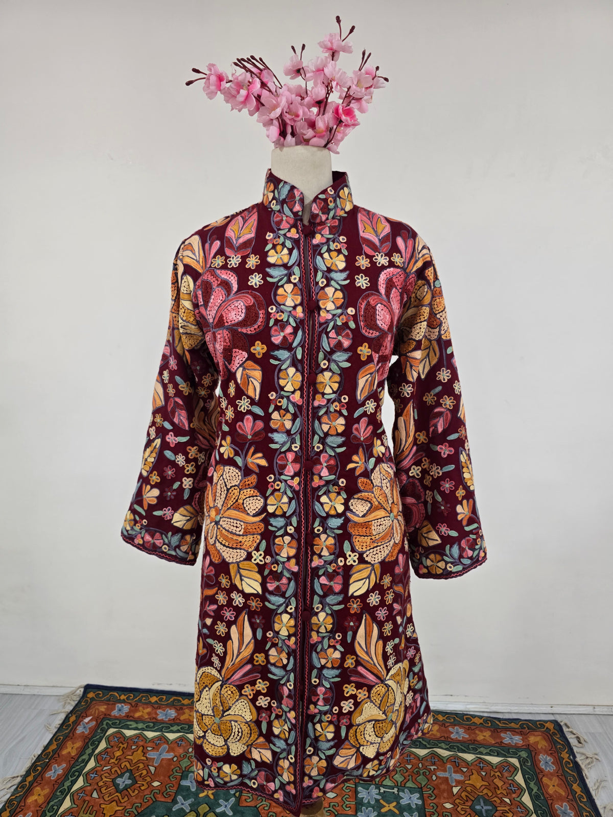 Full front view of a burgundy jacket on a mannequin, with colourful floral embroidery, long sleeves and a straight hem