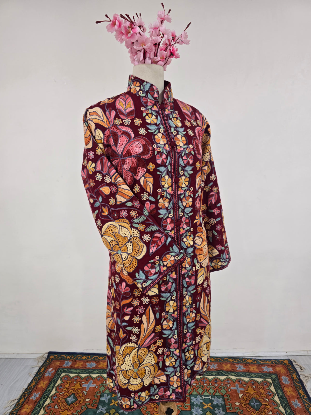 Angled view of the burgundy floral jacket with one sleeve crossed over the embroidered front
