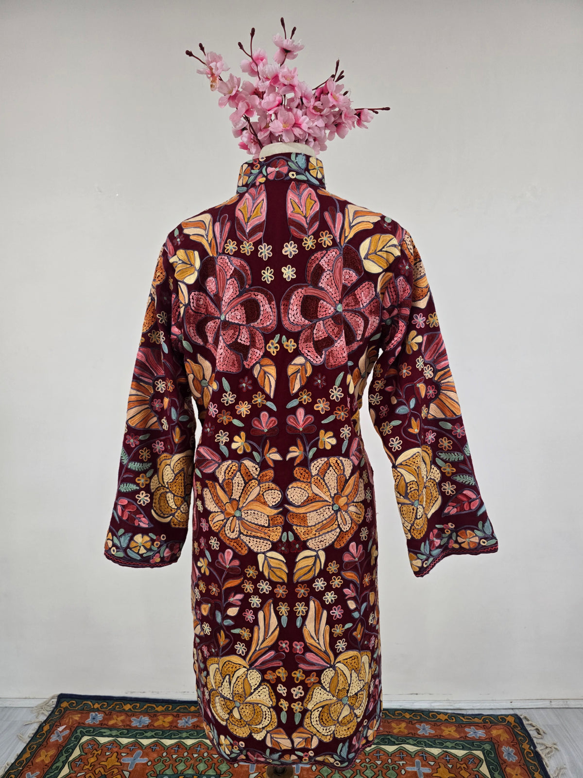 Back of the burgundy jacket, covered in symmetrical pink and gold flowers with teal leaf details