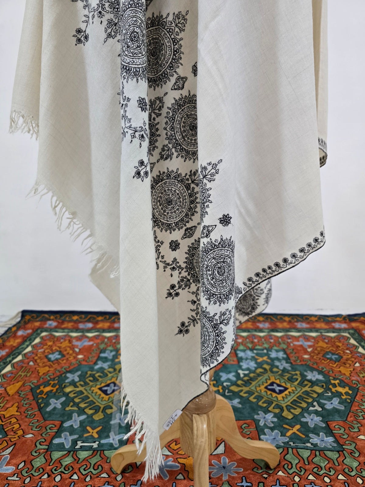 Ivory shawl folds showing black circular floral medallions, a narrow embroidered edge and short fringe