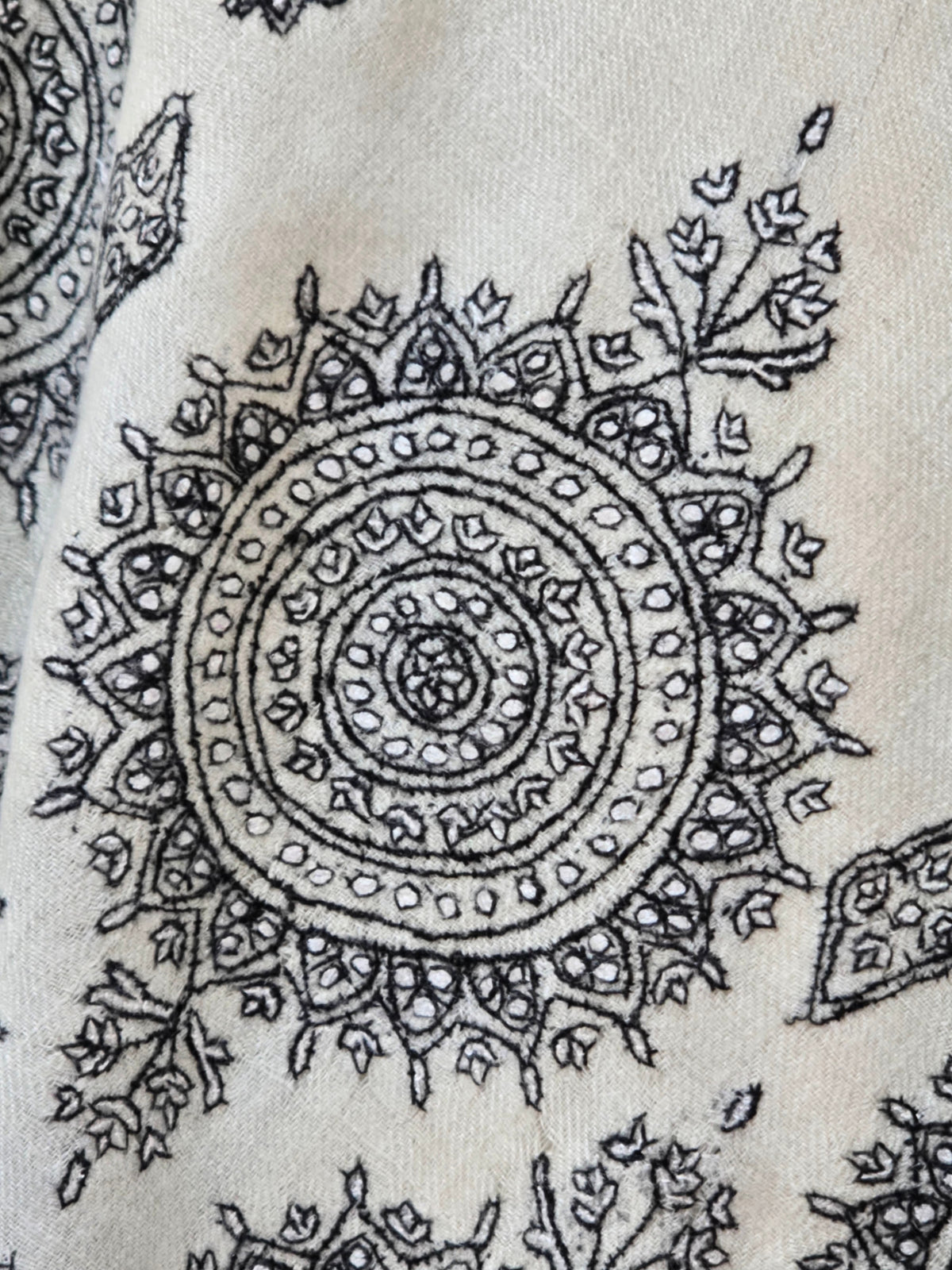 Close-up of a black circular embroidered medallion with fine leaves and floral sprigs on ivory