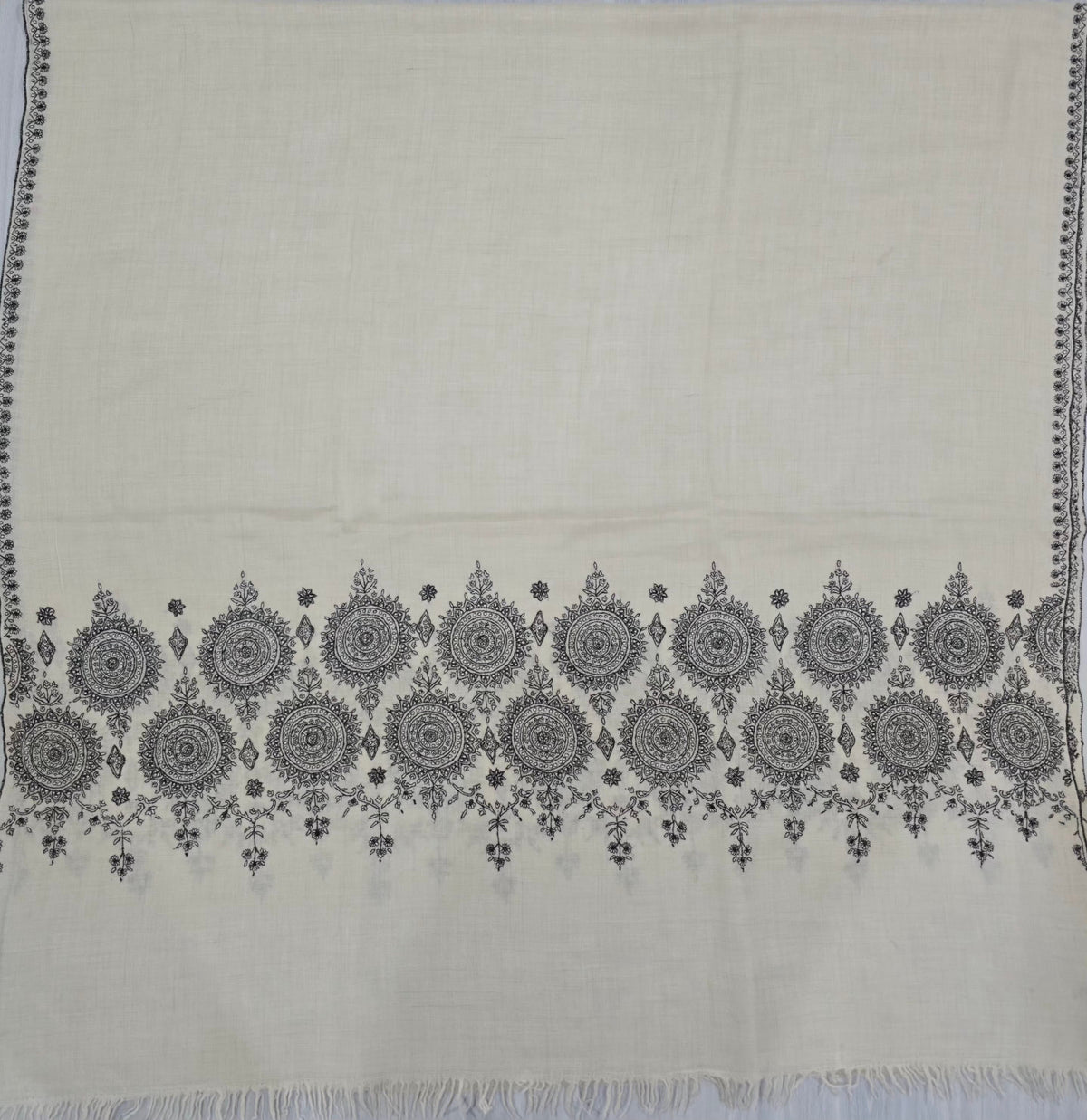 Ivory Pashmina shawl laid flat, with two rows of black floral medallions above a fringed end