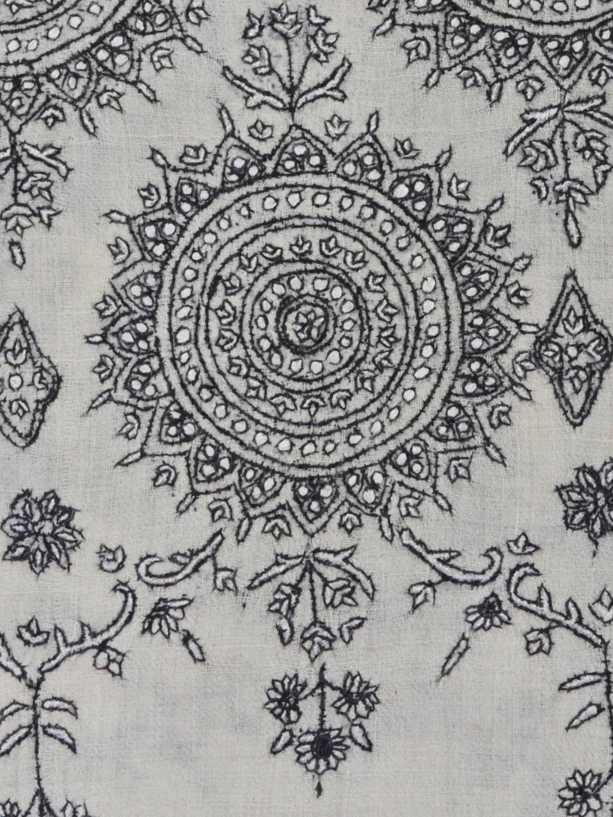 Close-up of fine black embroidery forming a circular medallion and trailing flowers on ivory