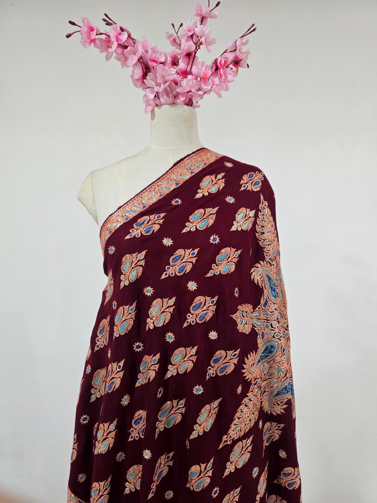 Garnet Pashmina shawl draped on a mannequin, with small gold motifs, turquoise and blue accents and a large floral medallion