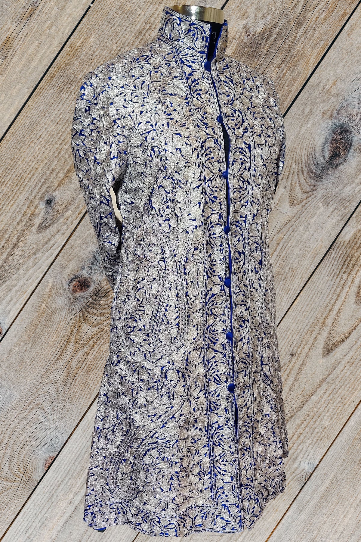 Angled front of the deep blue Noor-e-Gulzar jacket, showing silver-toned Aari flowers and a long bordered button opening.