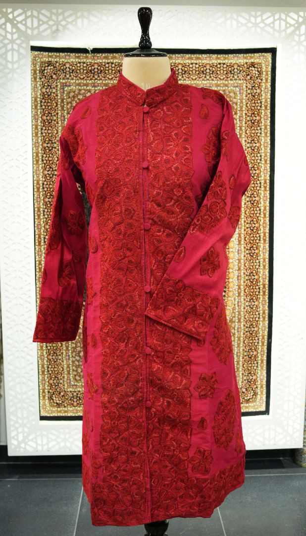Full front of the long ruby-red Aari jacket on a mannequin, showing dense embroidered borders and scattered sleeve motifs.