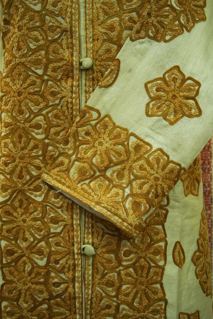 Close-up of the ivory jacket’s folded cuff over its buttoned front, showing gold Aari floral borders and a scattered flower motif.