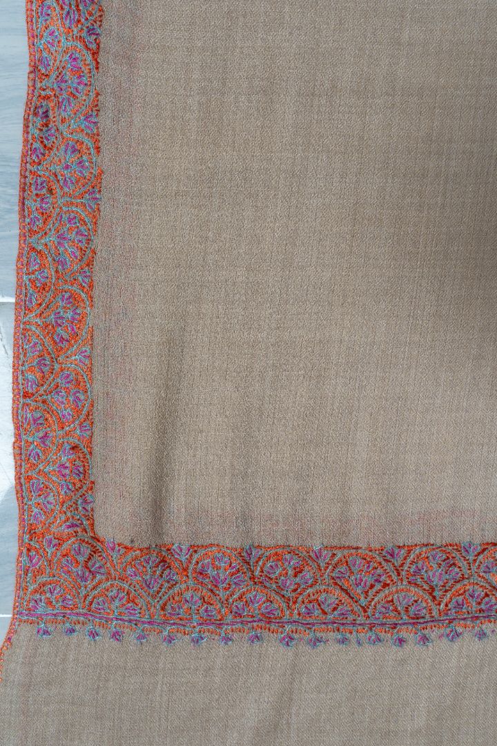 Flat corner of the beige shawl showing the red and turquoise floral border turning at a right angle