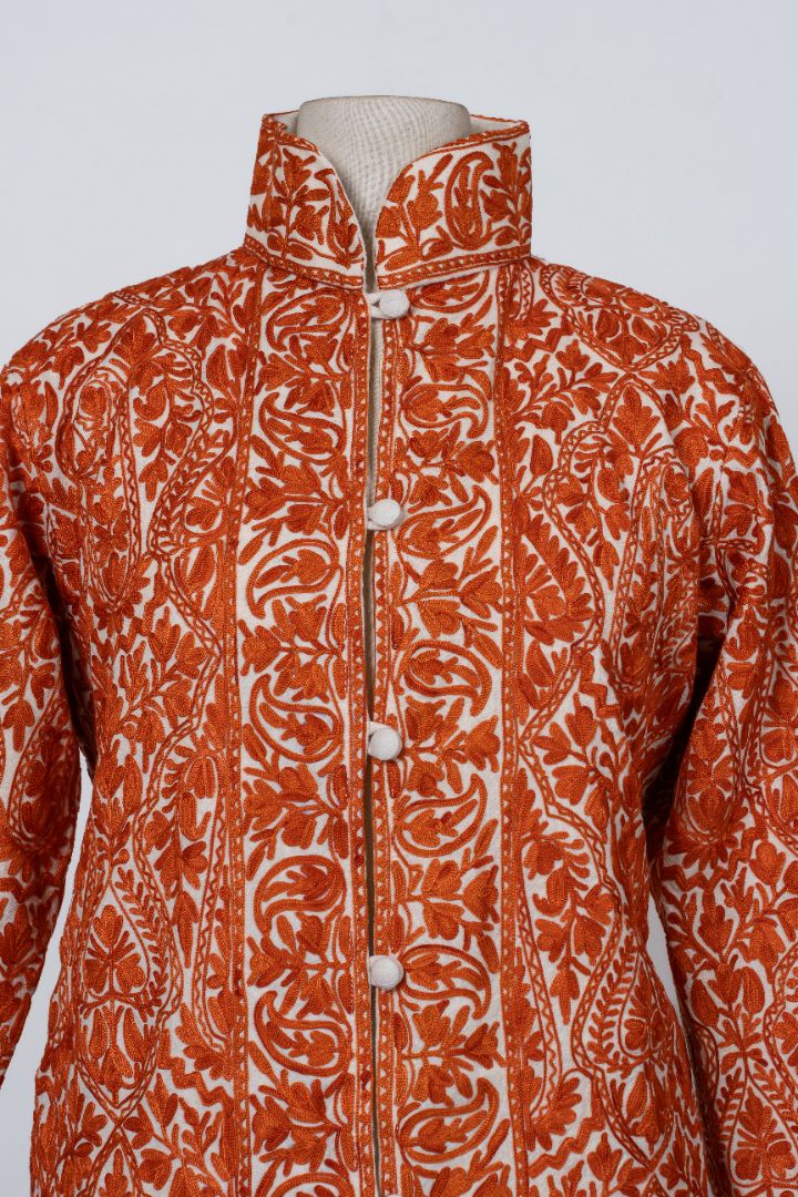 Upper front detail of the jacket with white covered buttons between orange floral bands and large paisley motifs.