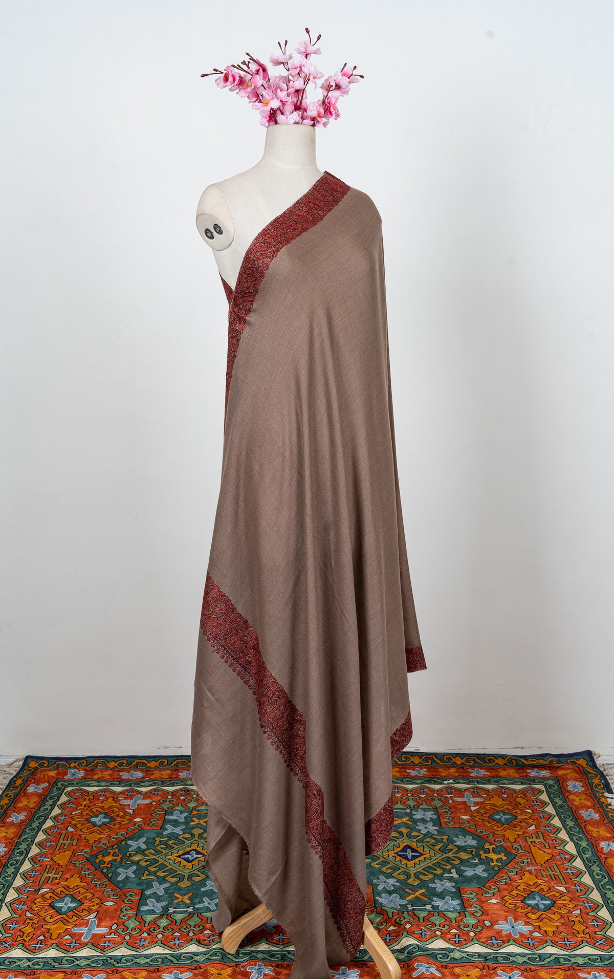 Full-length mocha-brown shawl draped on a mannequin, with rust embroidered borders around a plain field