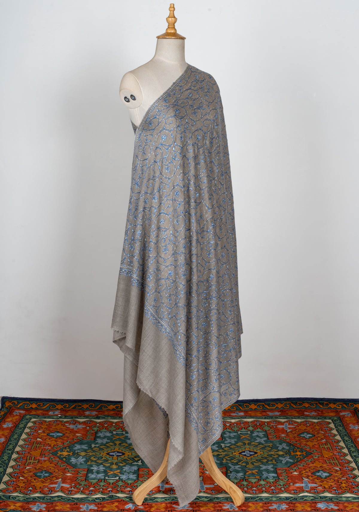 Full-length grey shawl on a mannequin, with blue Sozni floral vines, narrow borders and a plain grey end margin