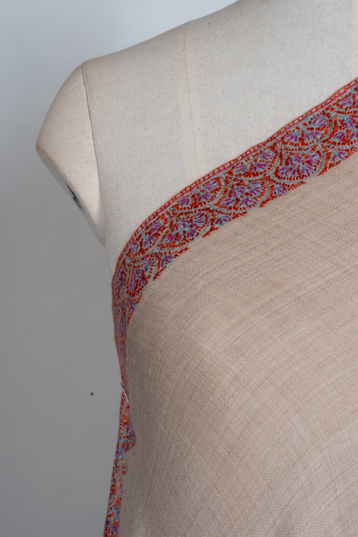 Close view of the red, turquoise and violet floral Sozni border along the beige shawl’s shoulder