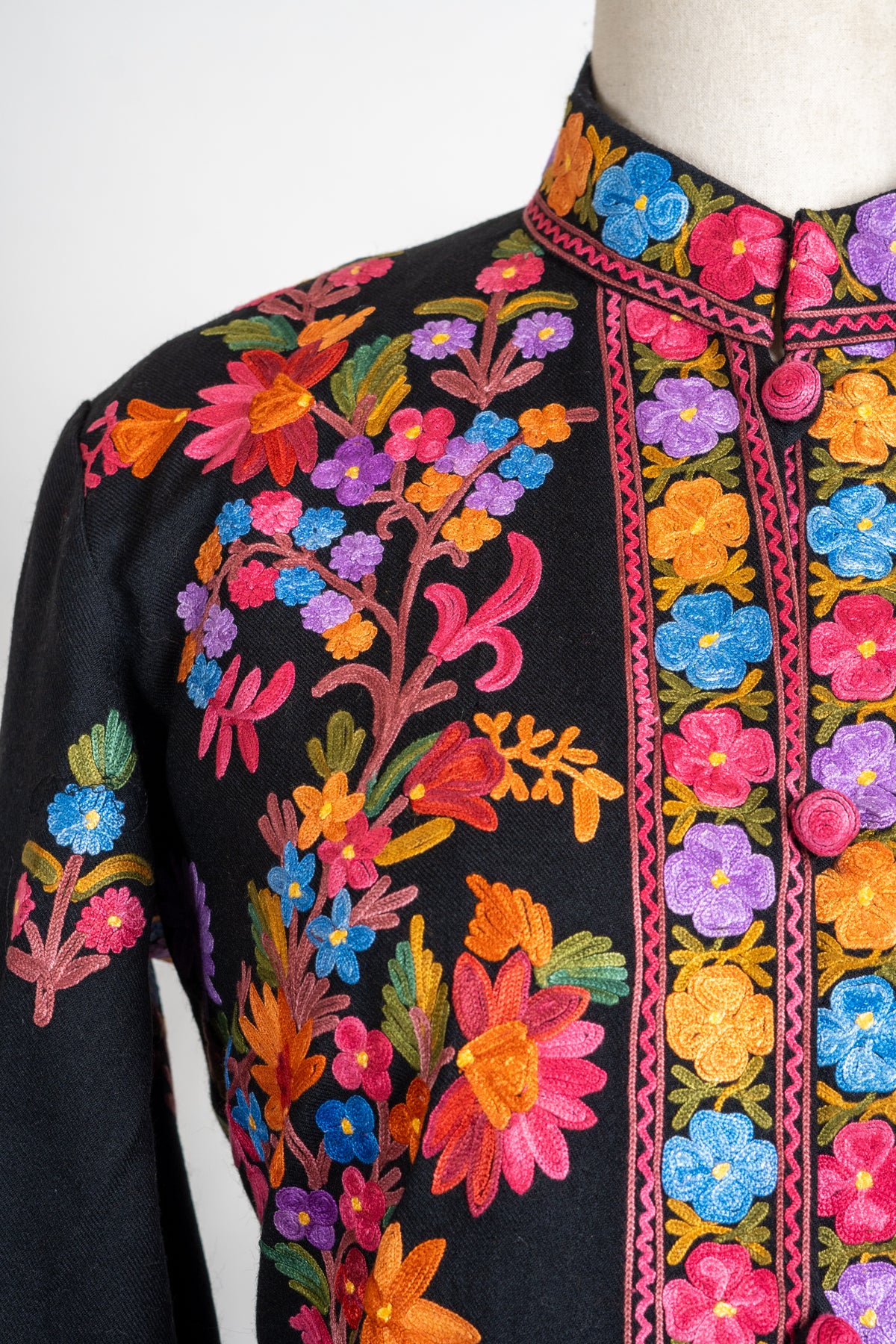 Shoulder and collar detail of the black jacket with bright floral Aari embroidery and pink edging.