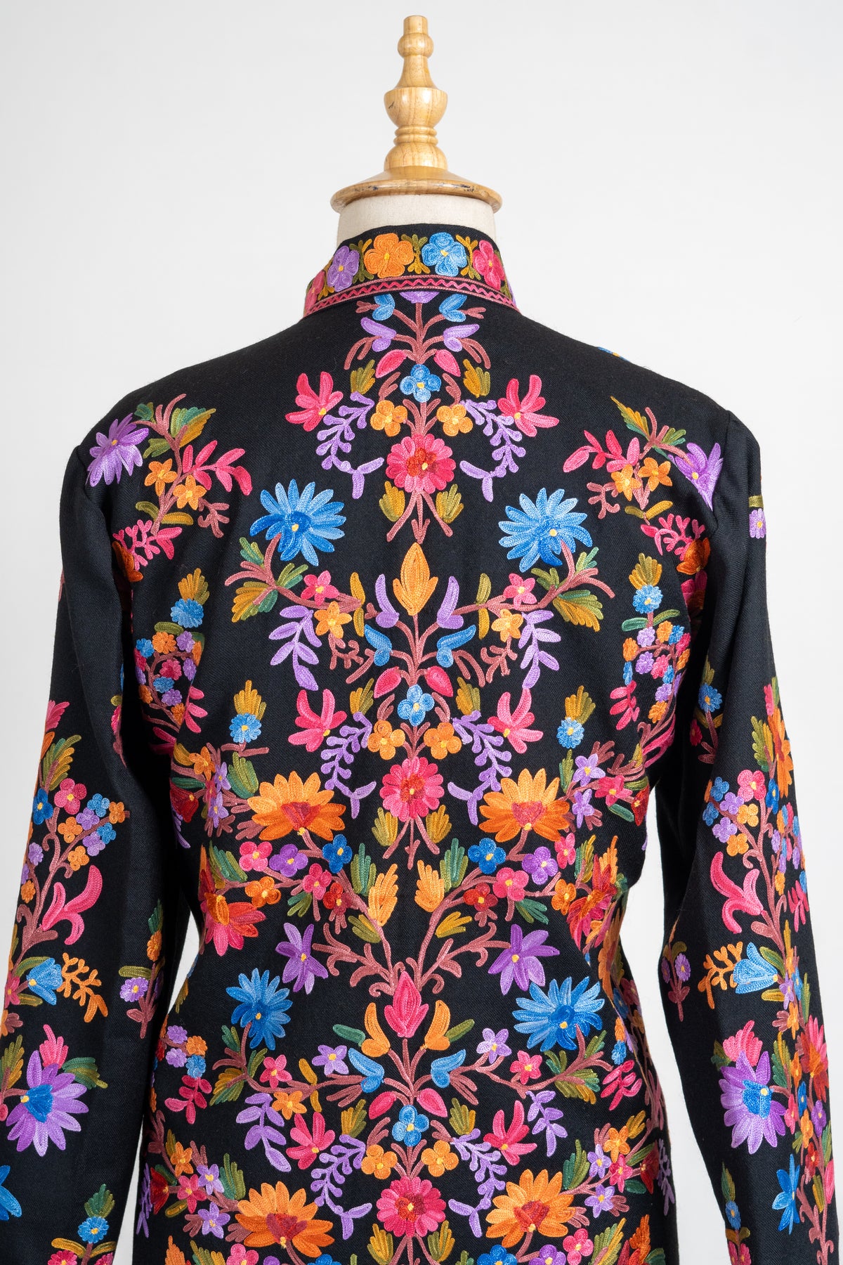 Rear collar and upper-back view of the black jacket with a symmetrical branching arrangement of colourful flowers.
