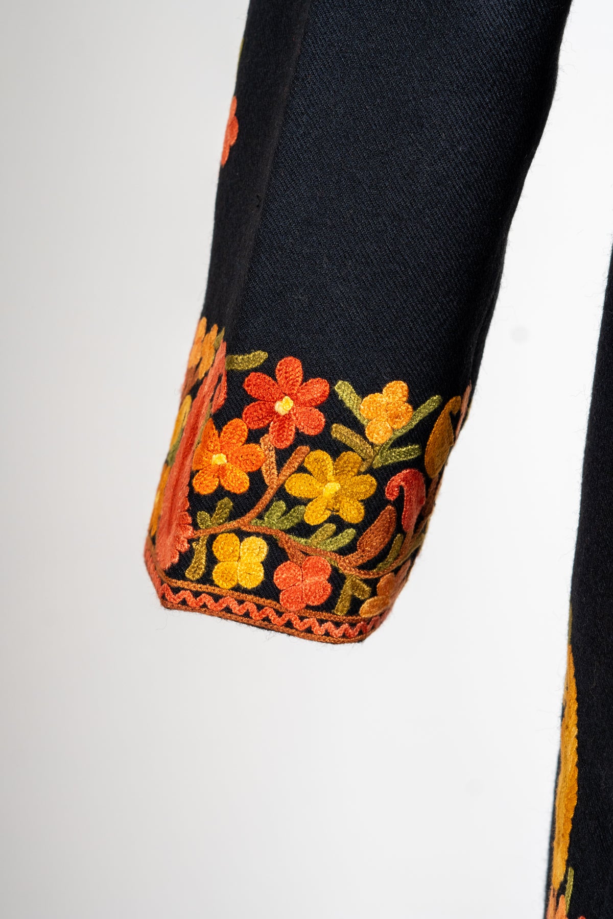 Black jacket cuff with golden and orange flowers, green leaves and a fine orange stitched edge