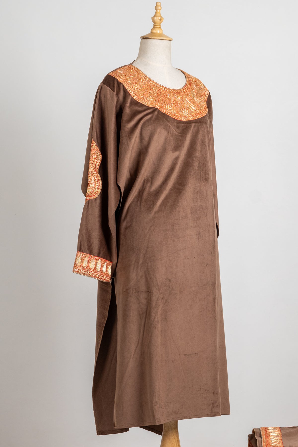 Angled full front of the brown velvet pheran, showing its gold-toned neckline, cuff embroidery and large sleeve motif.