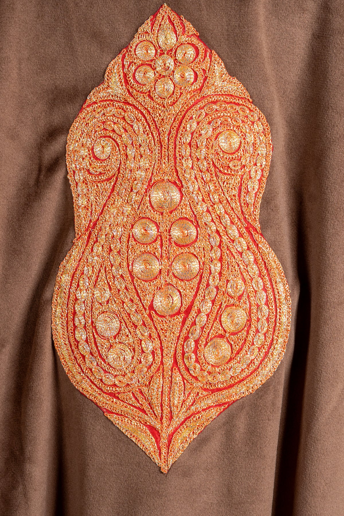 Close-up of the gold-toned Tilla back motif on brown velvet, with mirrored paisleys, floral circles and orange outlines.