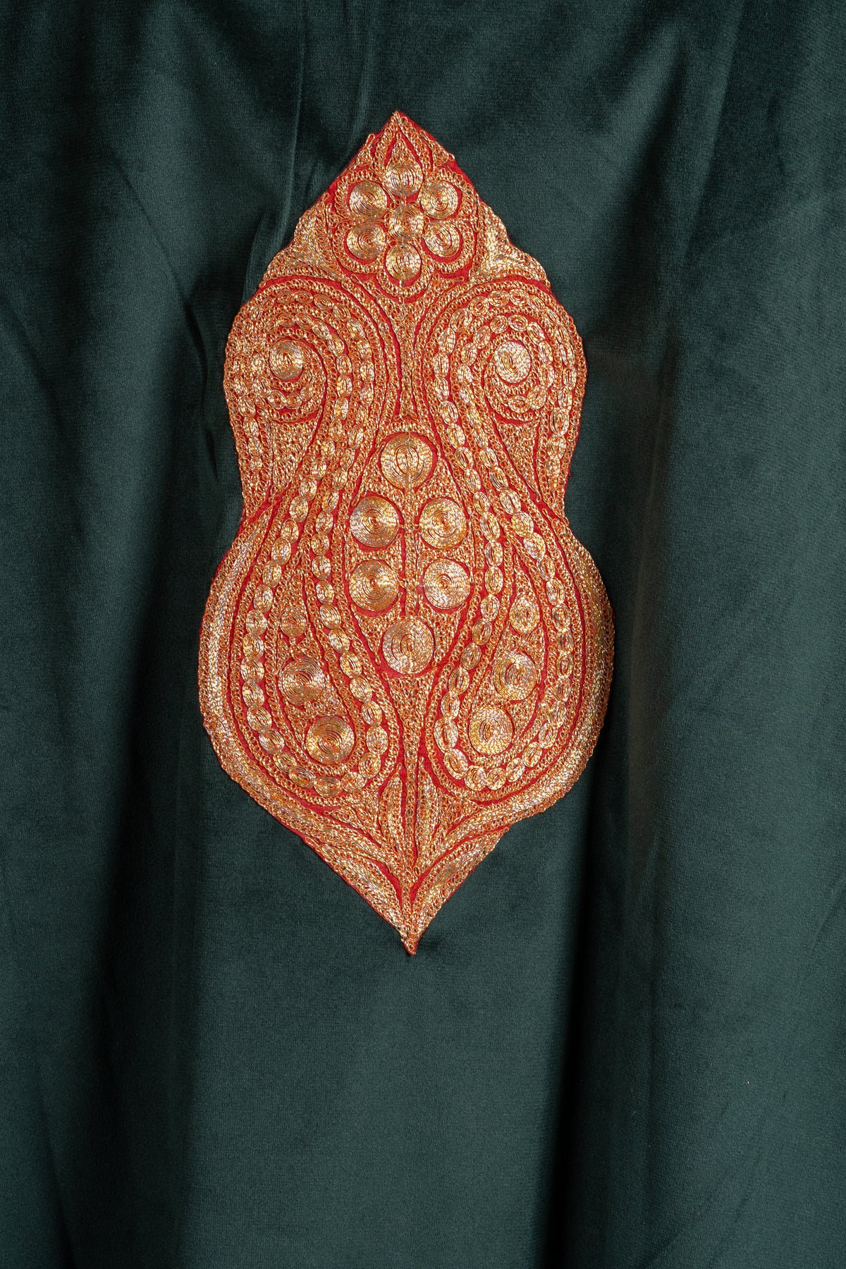 Close-up of a copper-gold Tilla medallion with paired paisleys and flowers on forest green velvet