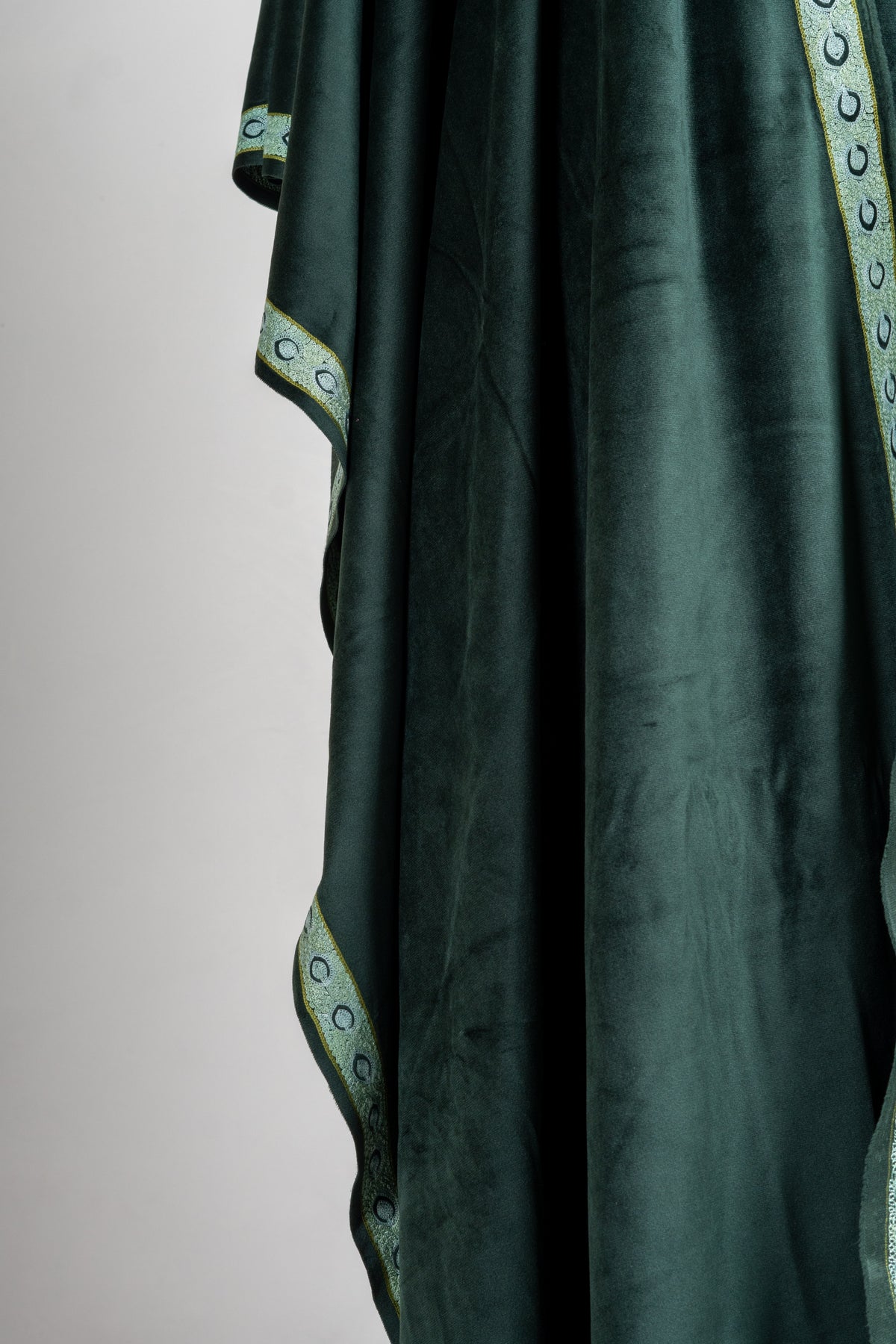 Long folds of a deep emerald velvet stole with a narrow pale green embroidered border along the edge