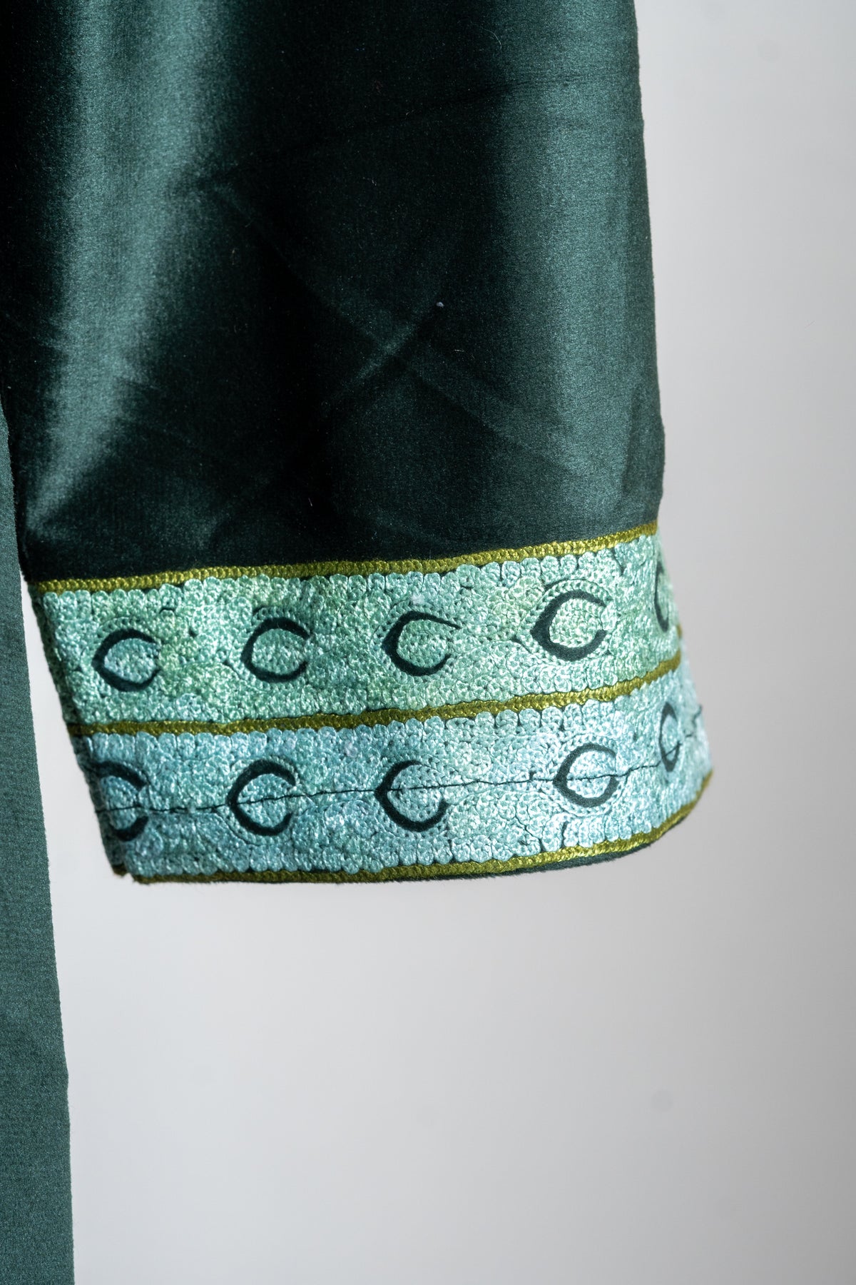 Close-up of the emerald velvet sleeve cuff with two pale green embroidered bands and dark curved motifs