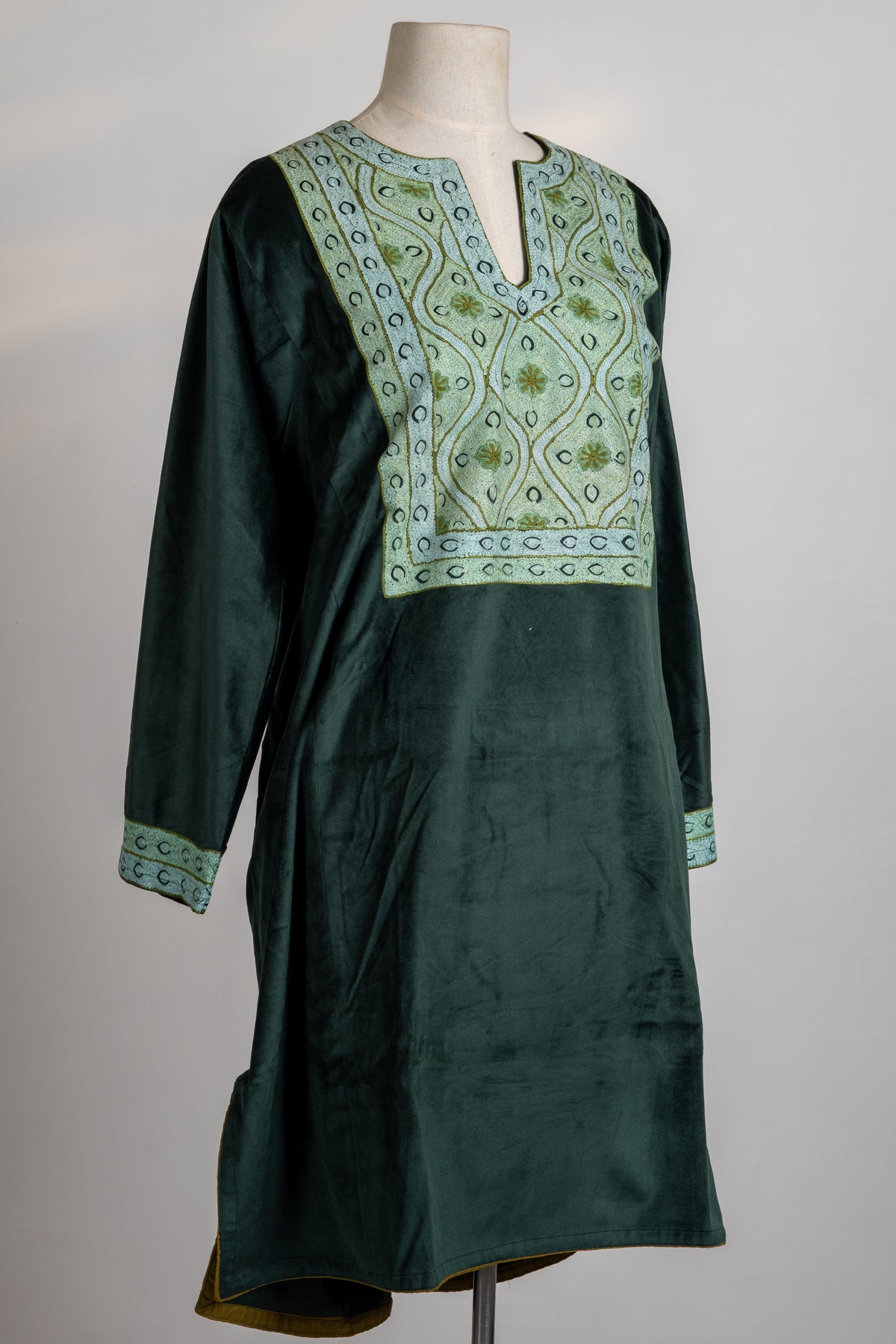 Angled full view of the deep green velvet suit top with a pale embroidered yoke, matching cuffs and side slits