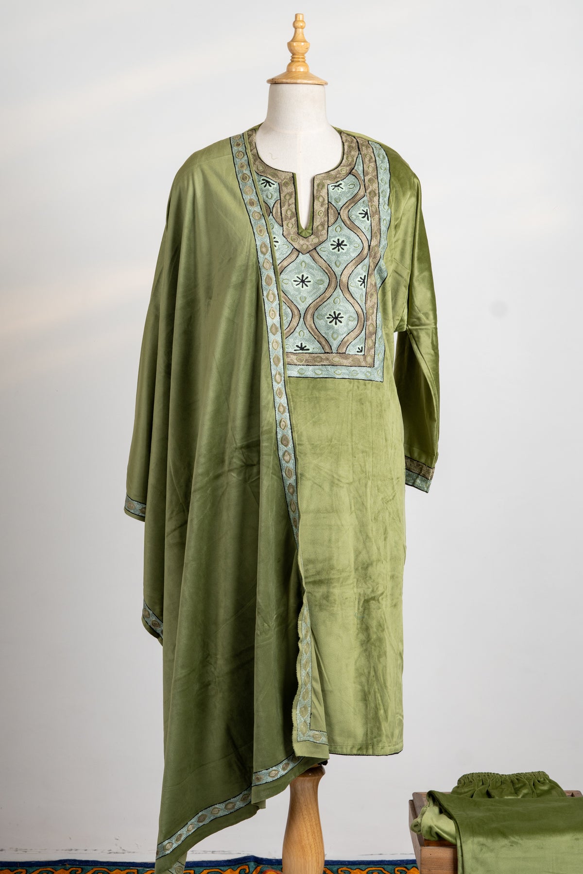 Full view of the olive velvet suit with an embroidered chest panel and matching bordered stole draped from one shoulder.