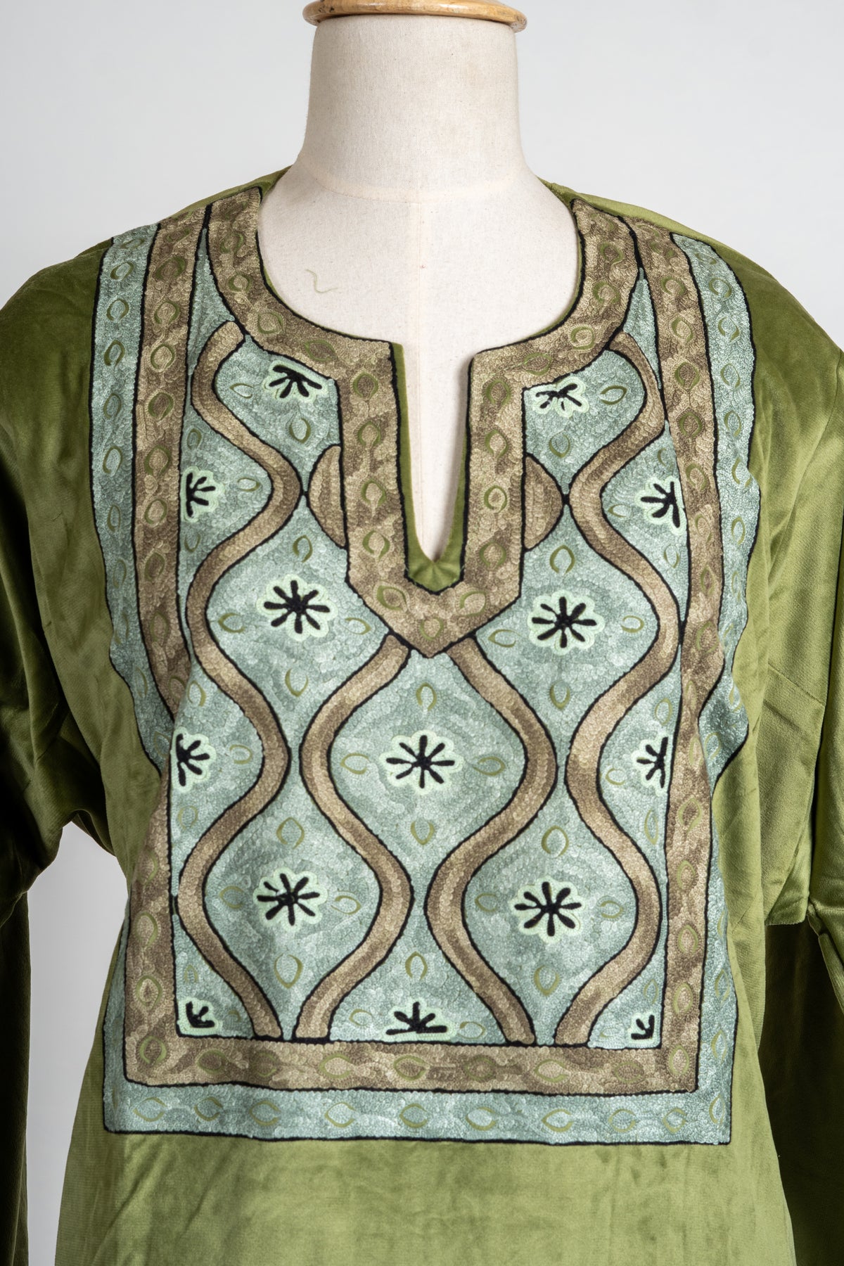 Close-up of the olive tunic neckline with pale blue and gold curving lattice embroidery and small dark floral motifs.