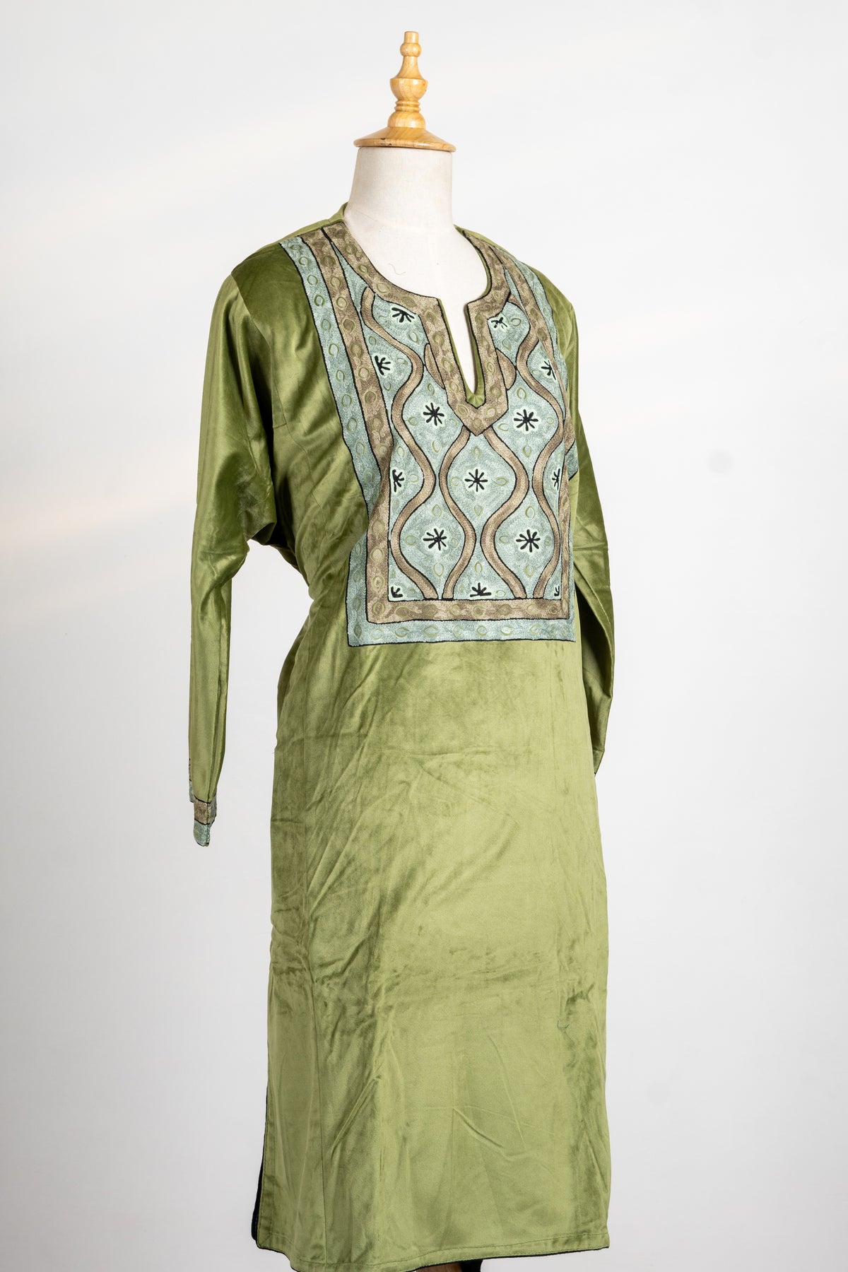 Angled view of the olive velvet tunic on a mannequin, with a rectangular embroidered chest panel and matching cuff trim.