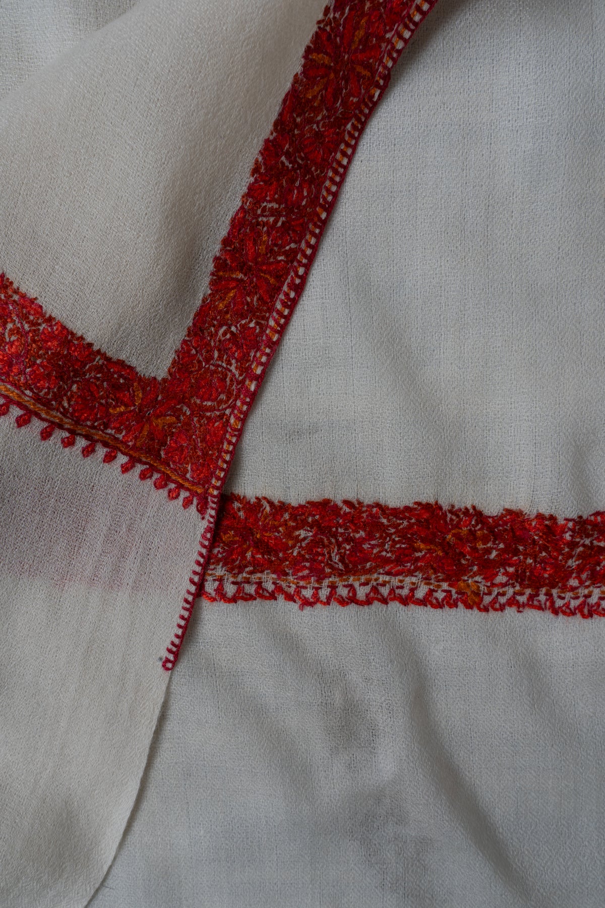 Folded corner of an ivory shawl showing the front and reverse of its crimson embroidered border