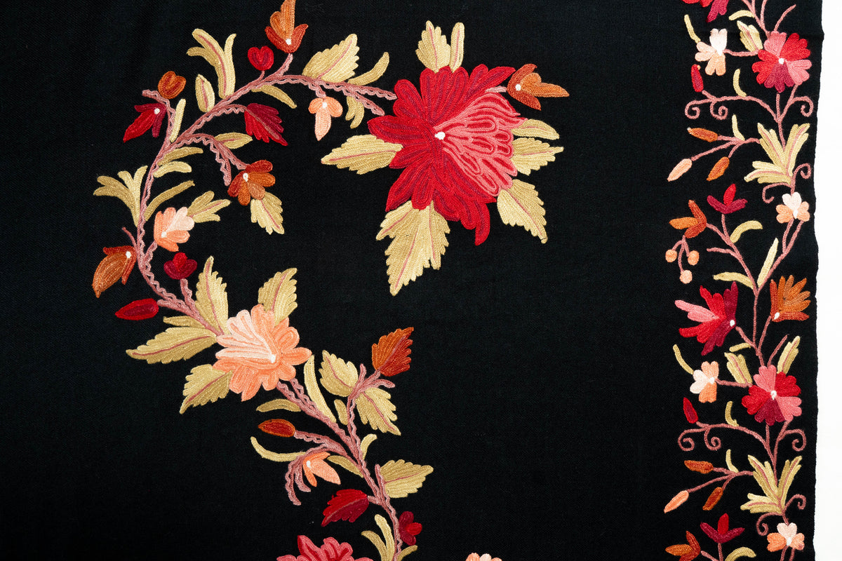 Flat detail of a curling red and peach Aari floral garland beside the black stole’s matching flower border.