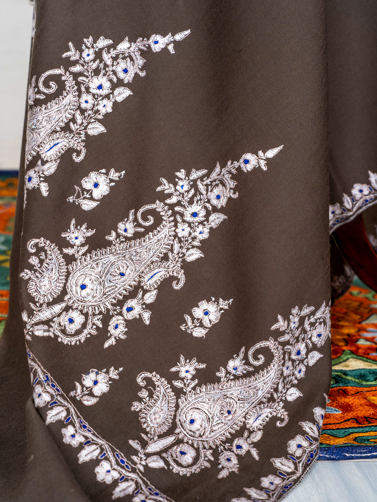 Close-up of ivory Sozni paisleys and floral sprays with tiny blue accents on the mocha-brown Pashmina shawl