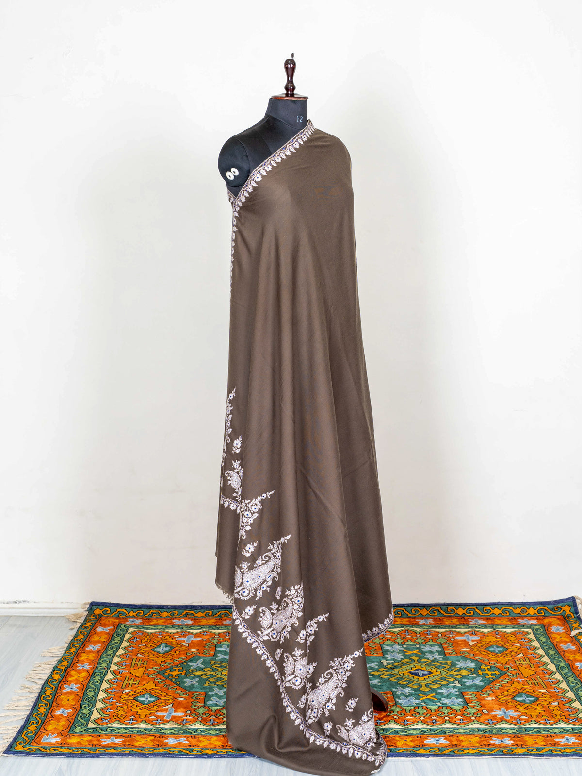 Mocha-brown Pashmina shawl draped over one shoulder, with a plain centre and ivory Sozni embroidery near the lower edge