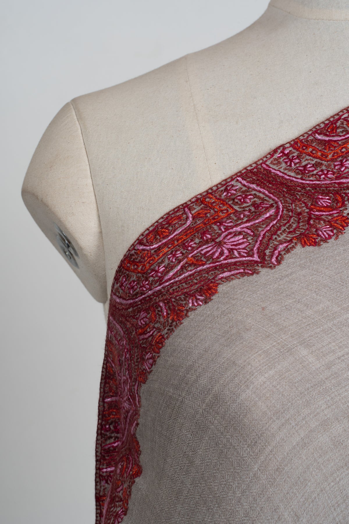 Shoulder close-up of the grey shawl with crimson and pink floral embroidery inside repeated pointed arches.